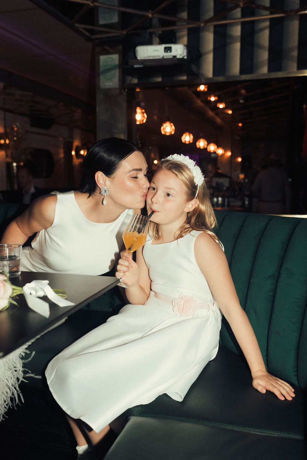 A parent and child in white outfits share tender moments while dancing at a celebration.