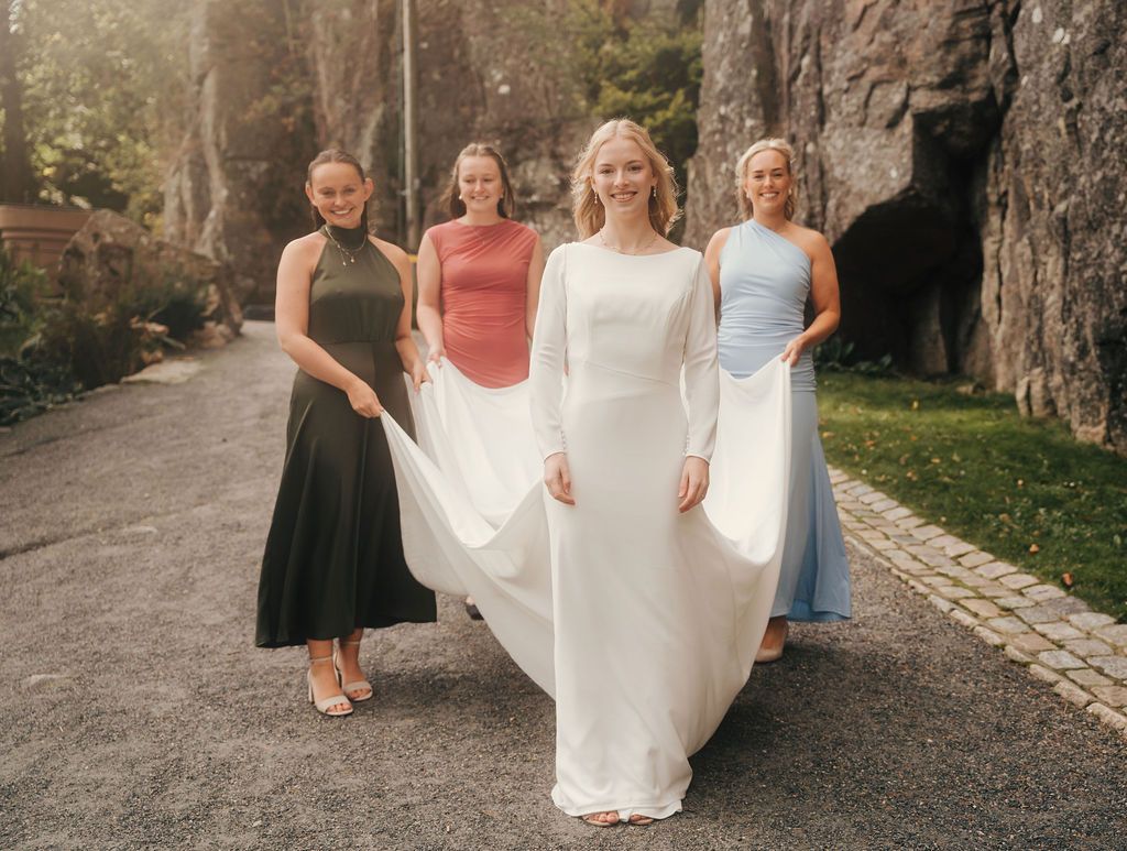 A group walks down a stone path while holding the train of a flowing white wedding dress.