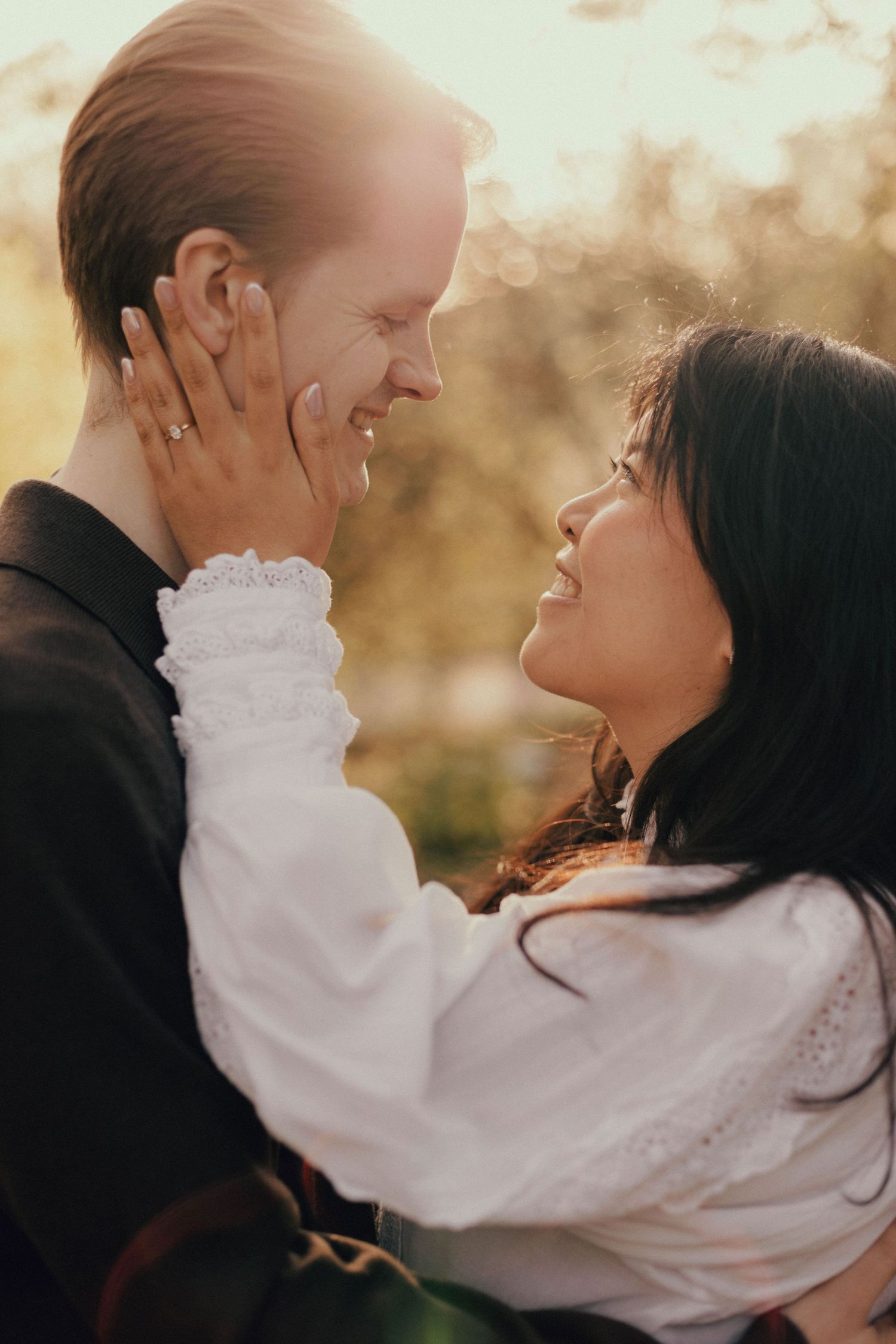 A romantic couple embraces in soft golden sunlight wearing white and black formal attire.