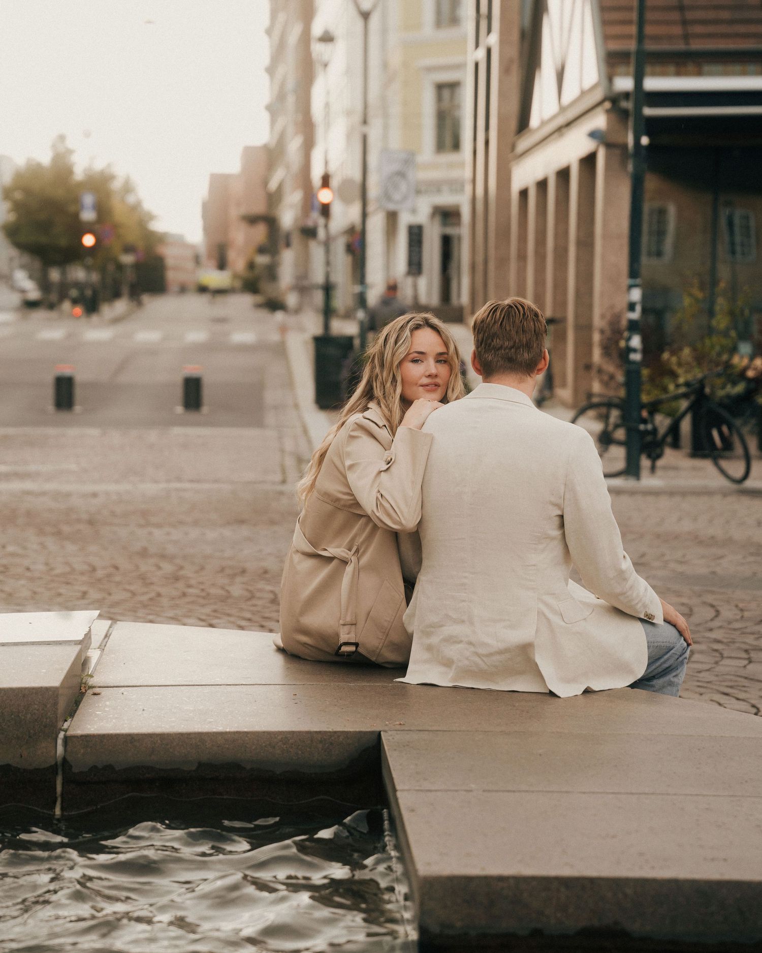 A couple sits together on stone steps in a European city street during autumn.