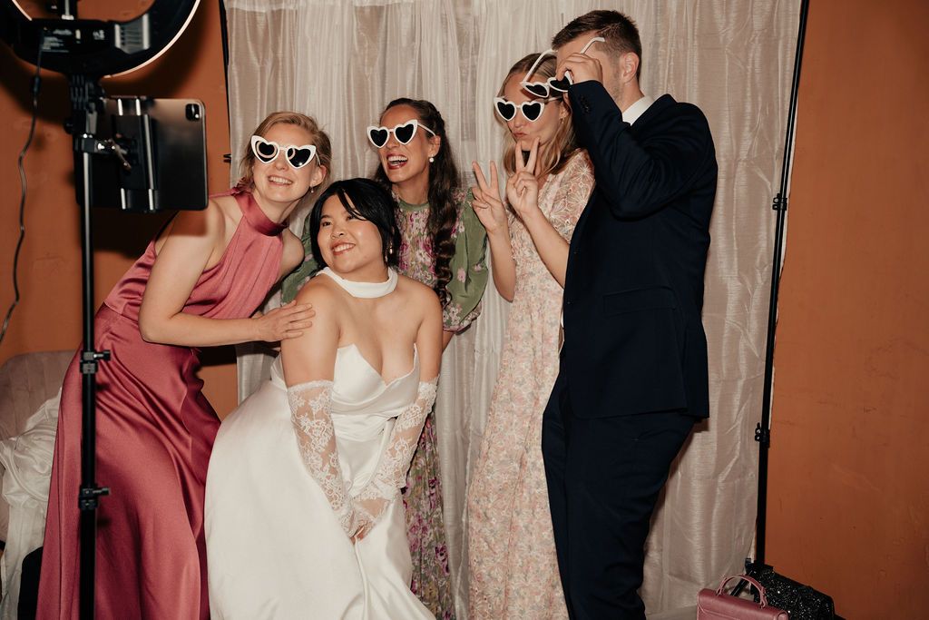 Wedding party guests wearing sunglasses dance and celebrate on a dance floor at an indoor reception.