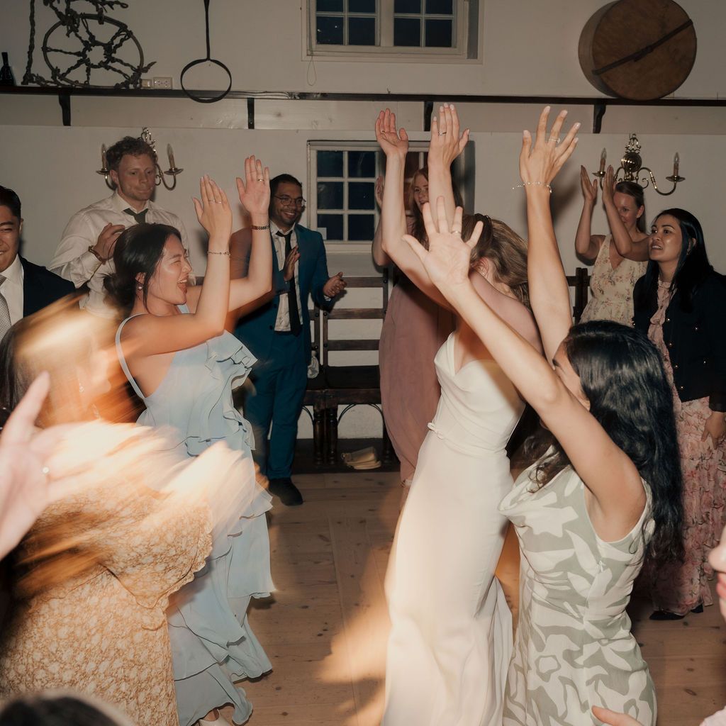 Wedding reception guests dancing together in a ballroom with joyful energy and raised hands.