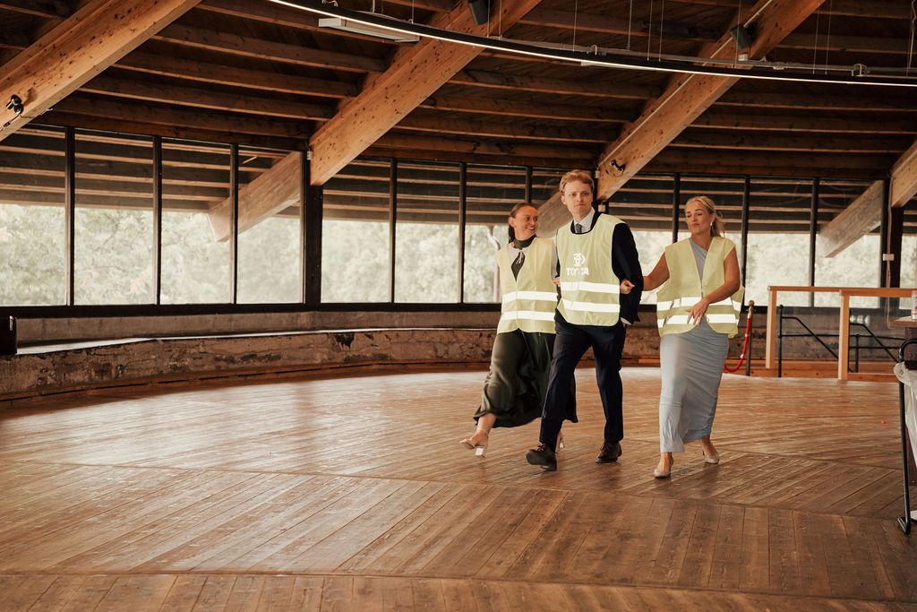 Dancers practice in a spacious wooden-floored studio with exposed ceiling beams and natural lighting.