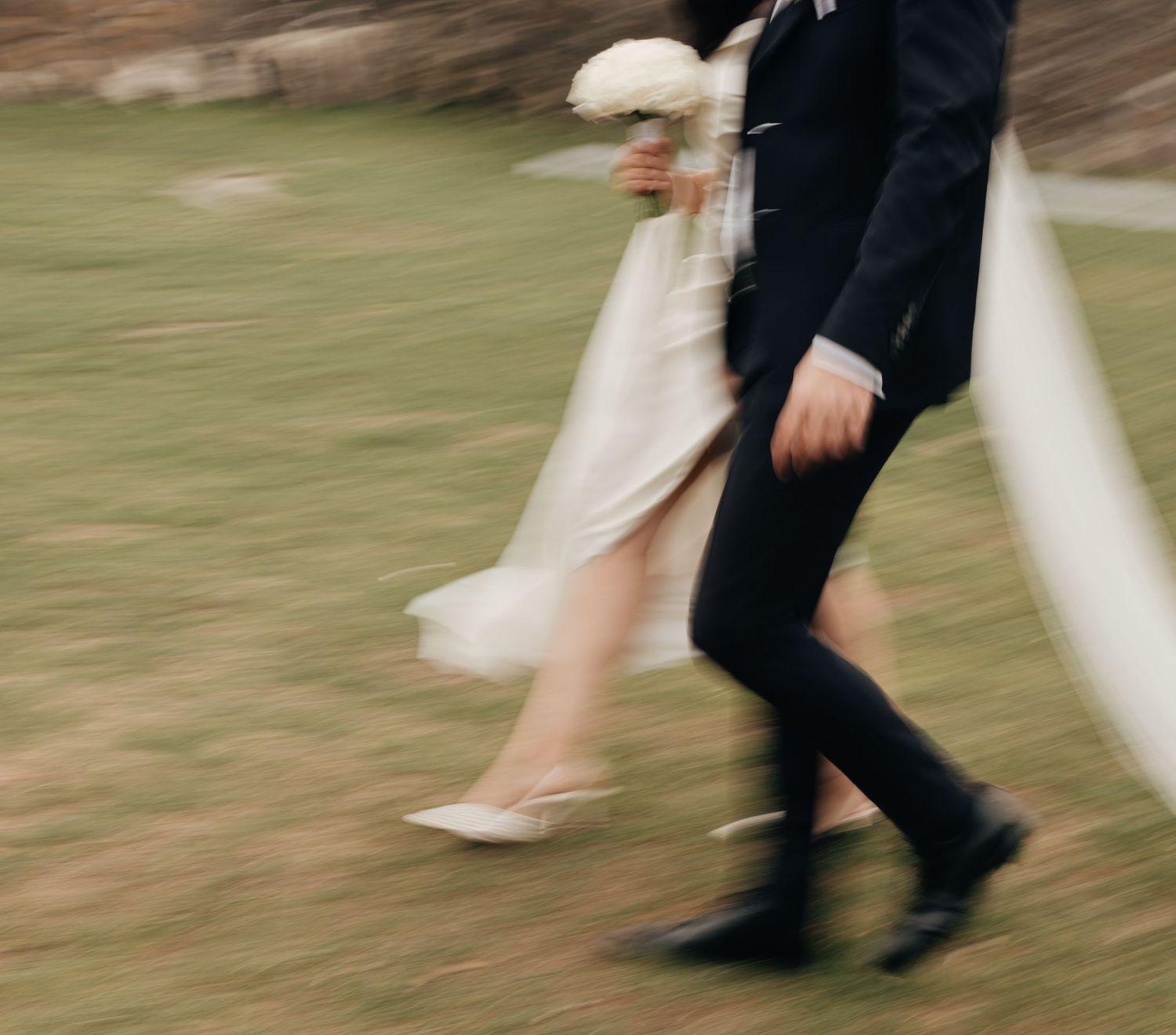Motion-blurred figures in formal attire walk across a green lawn at an outdoor event.