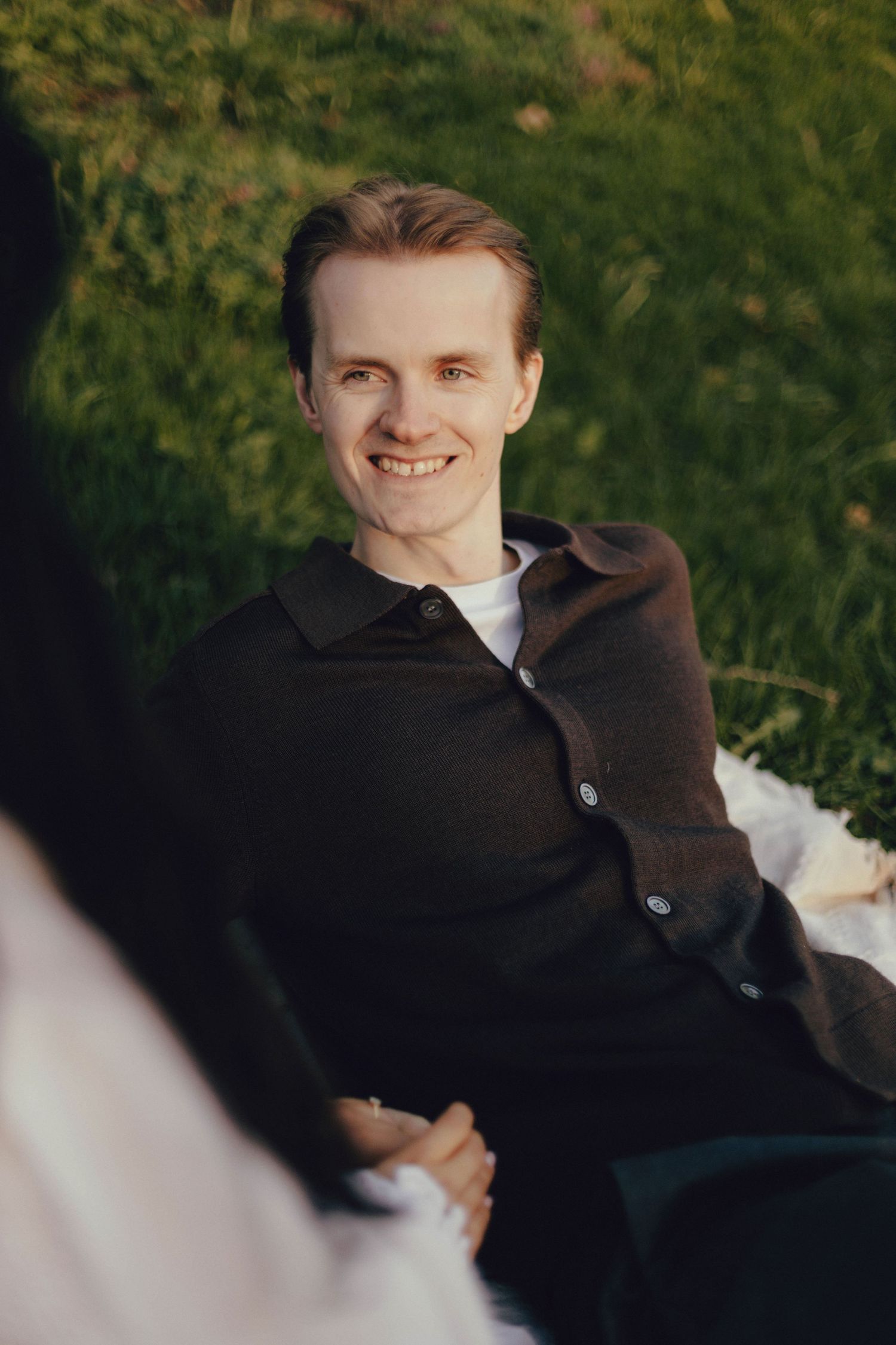 A person smiles warmly while reclining outdoors on a sunny day.