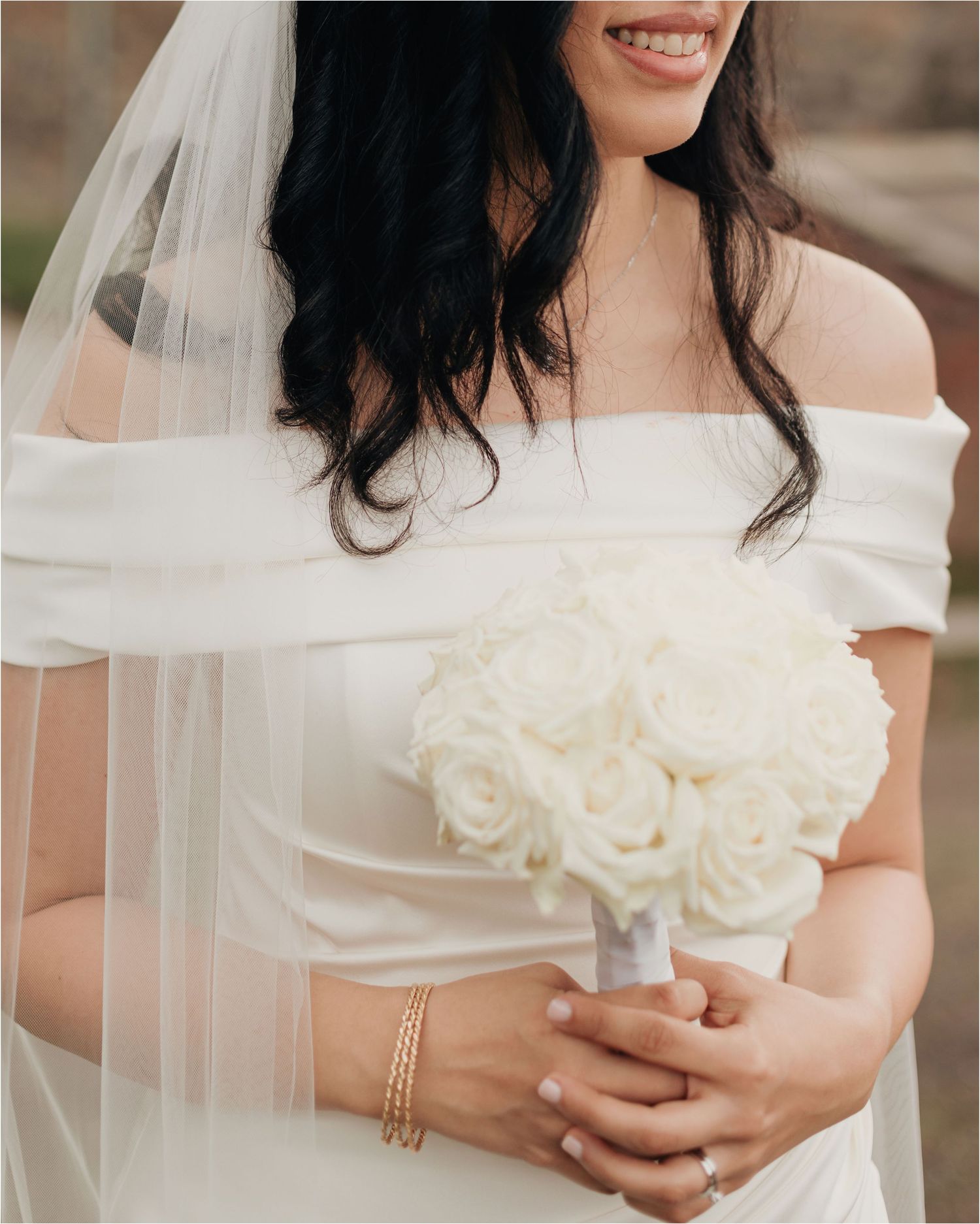 Close-up view of a bridal bouquet with white roses held against a white wedding dress.