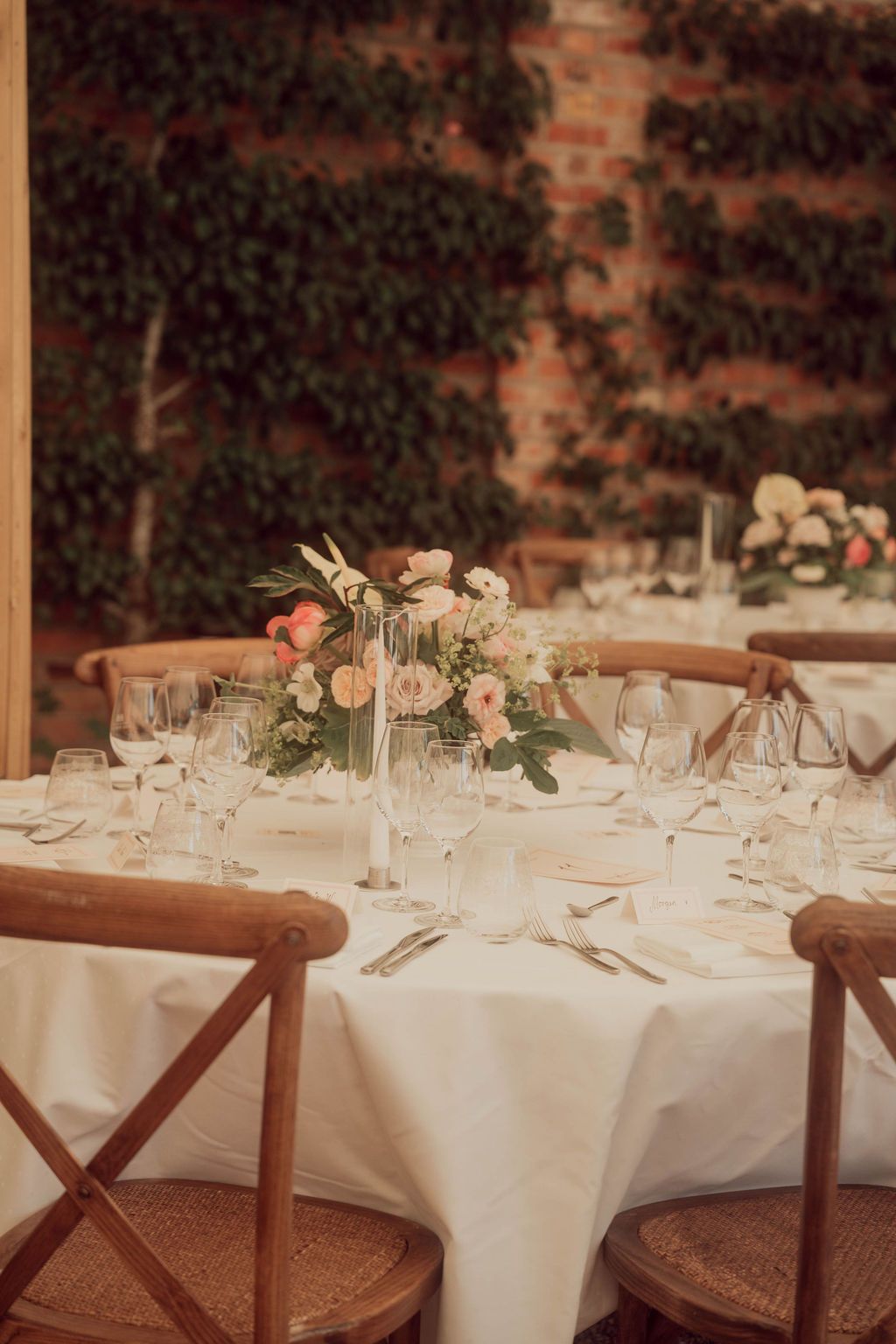 Elegant wedding reception table settings with white linens, rattan chairs, and soft peach floral centerpieces.