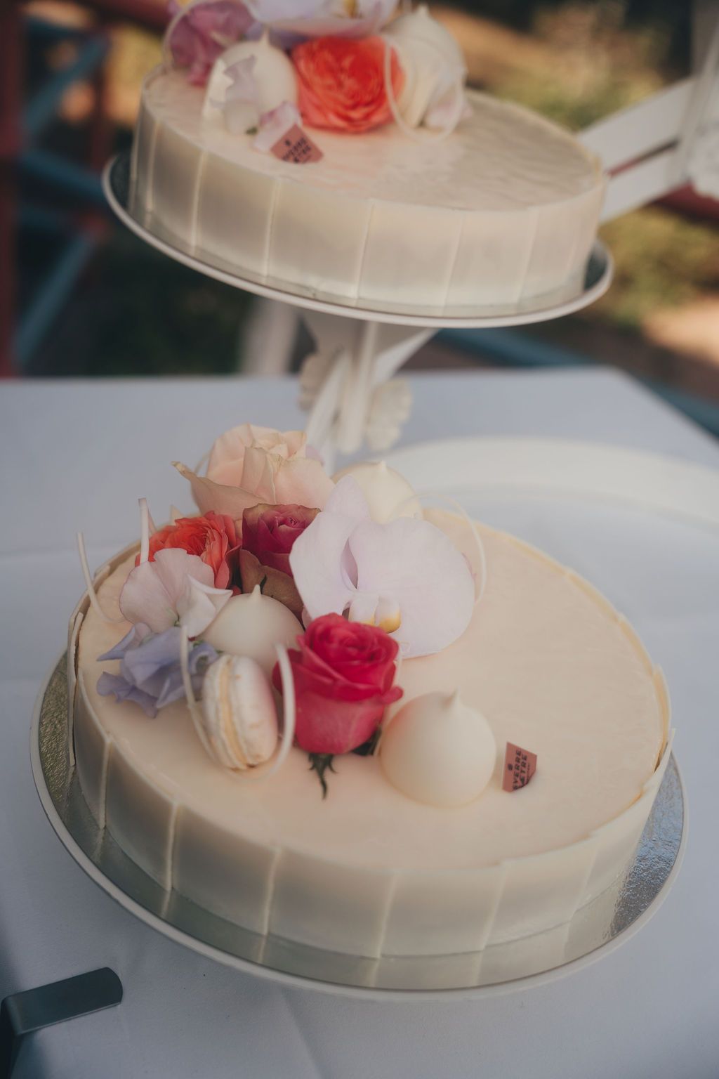 White frosted wedding cake decorated with delicate pink and red roses and petals on a silver cake stand.