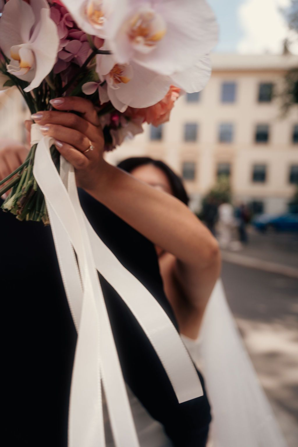 Delicate pink orchids tied with flowing white ribbons create an elegant bridal bouquet against an urban backdrop.