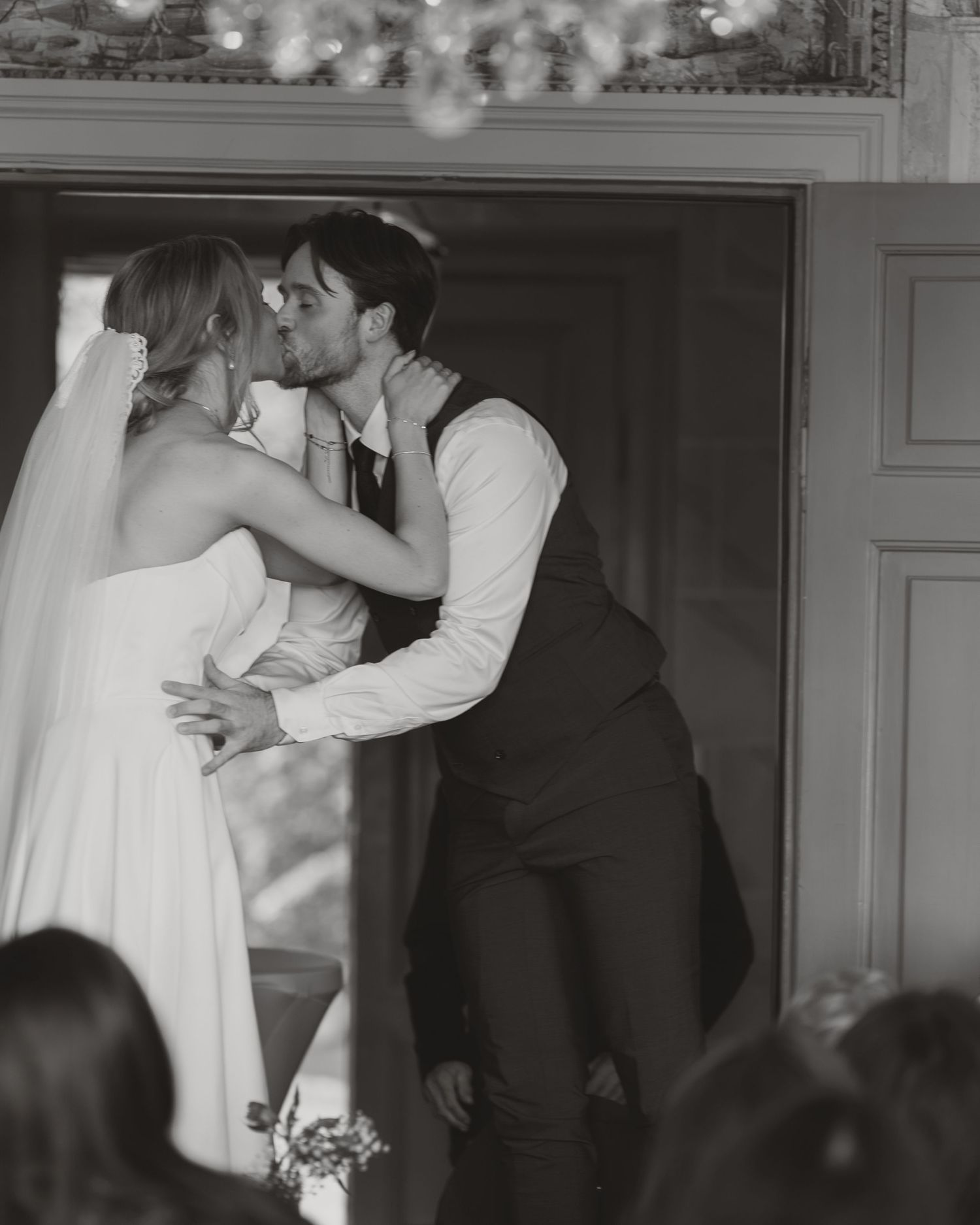 Black and white photo of a bride and groom sharing their first kiss at a wedding ceremony.
