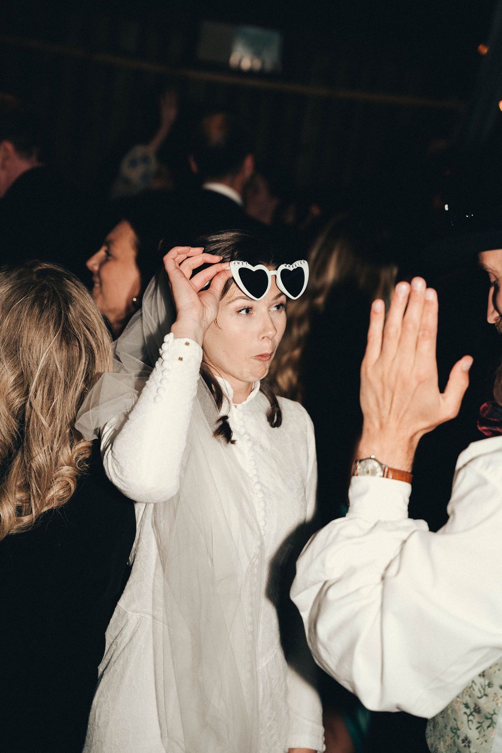 People in white clothing dance and raise their hands at a dimly lit party or celebration event.