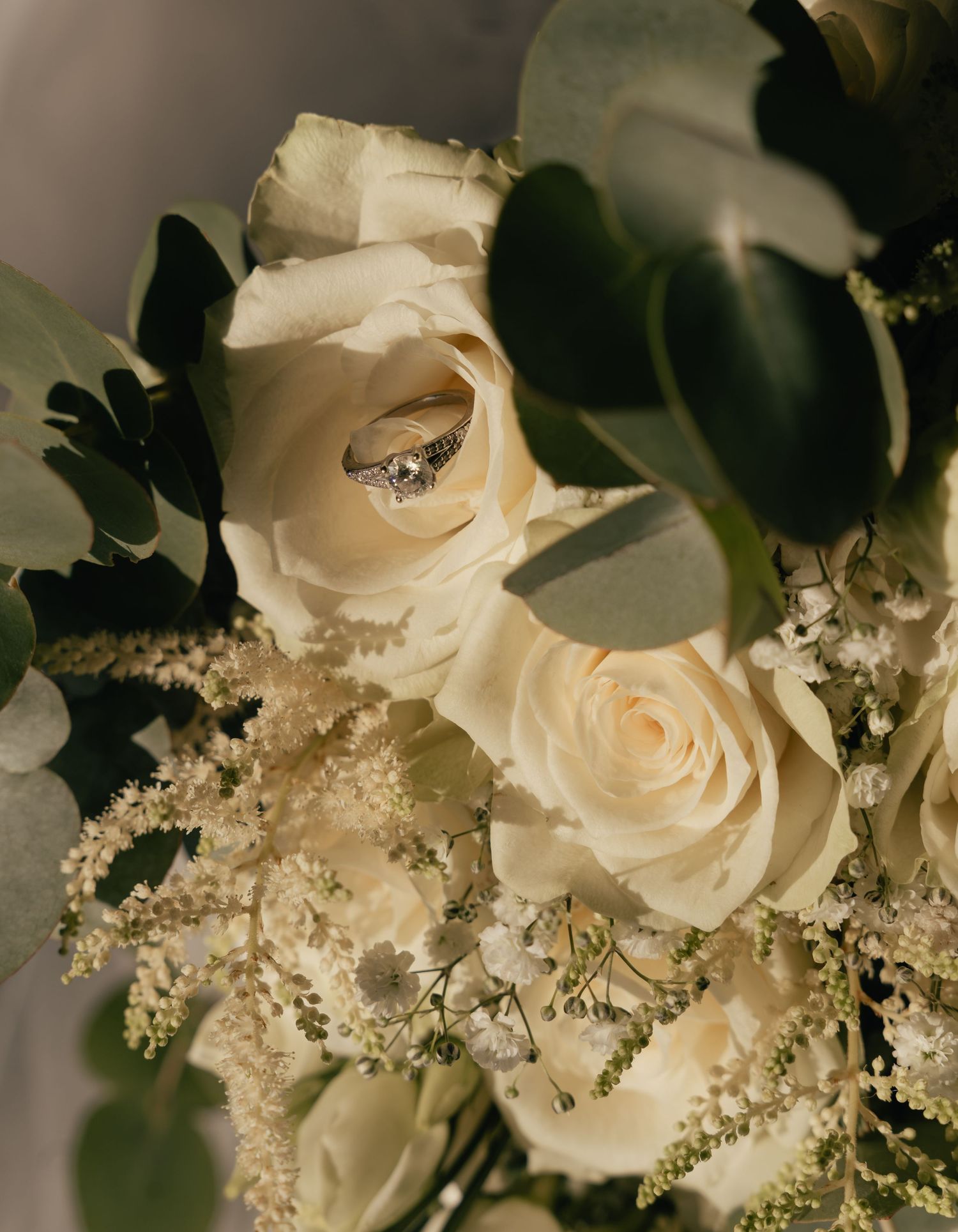 Diamond engagement ring nestled among white roses and eucalyptus in a bridal bouquet.