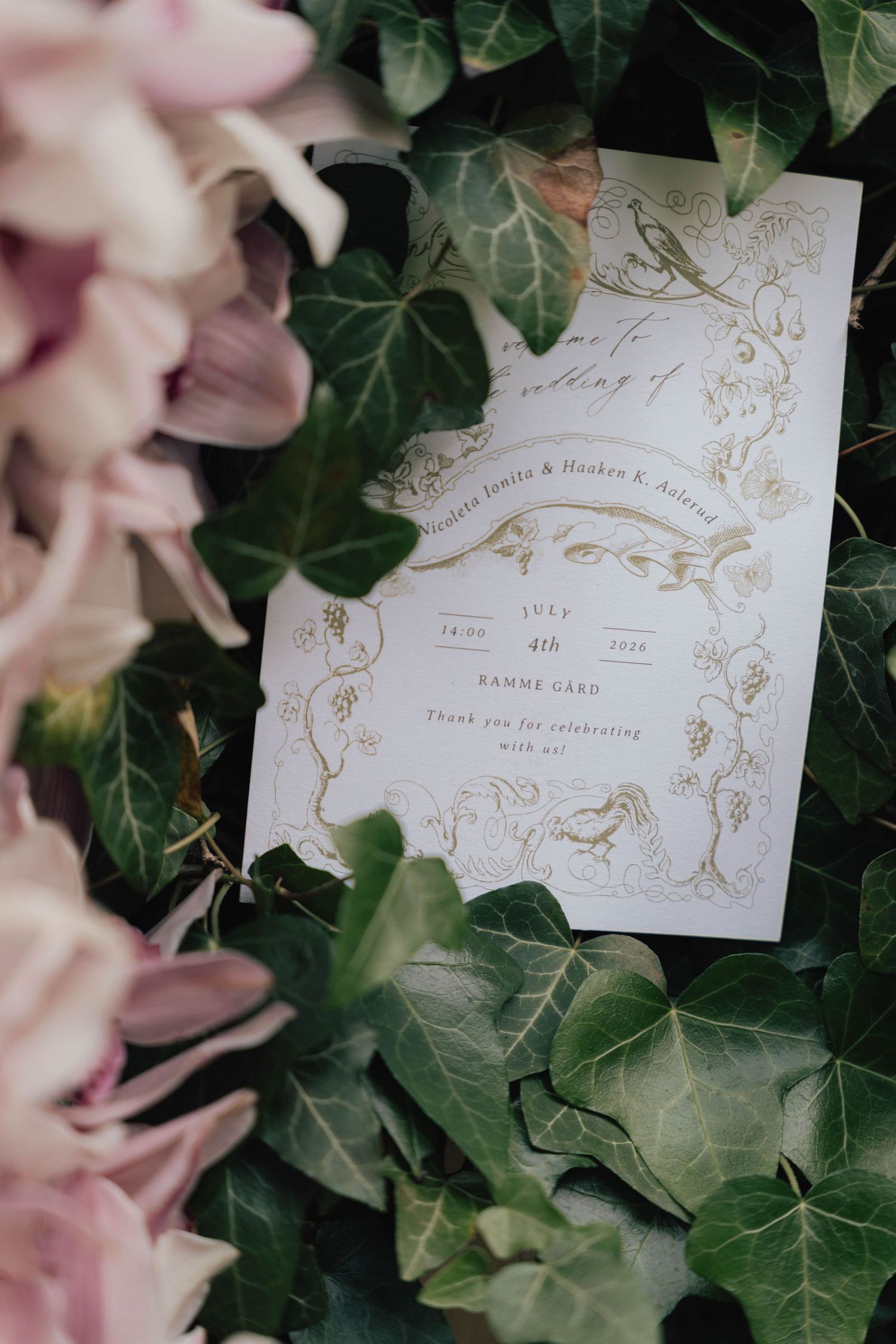 Elegant wedding invitation with gold botanical details, surrounded by lush ivy and soft pink flowers.