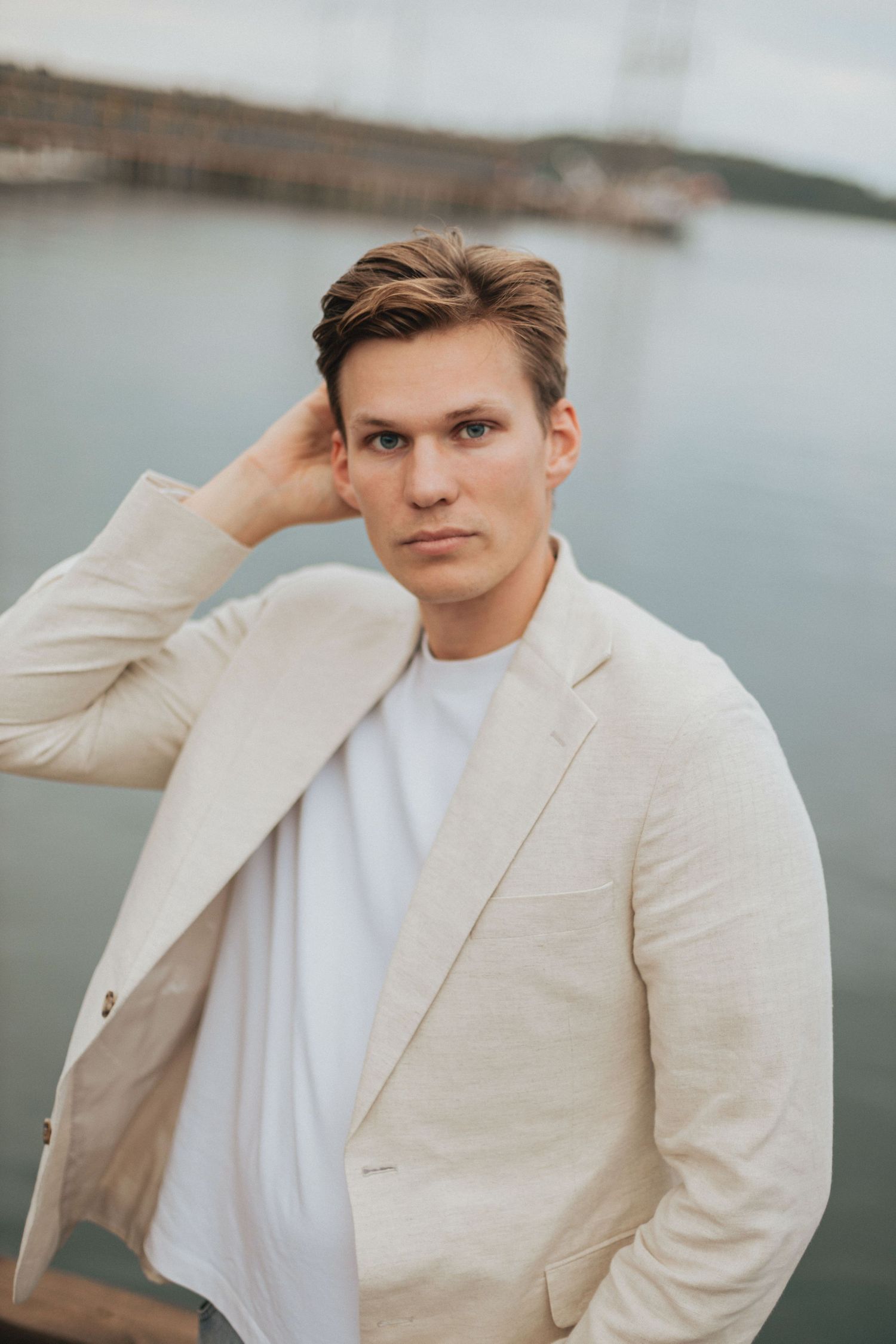 A person in a beige linen suit jacket and white shirt poses against a waterfront background in multiple portrait shots.
