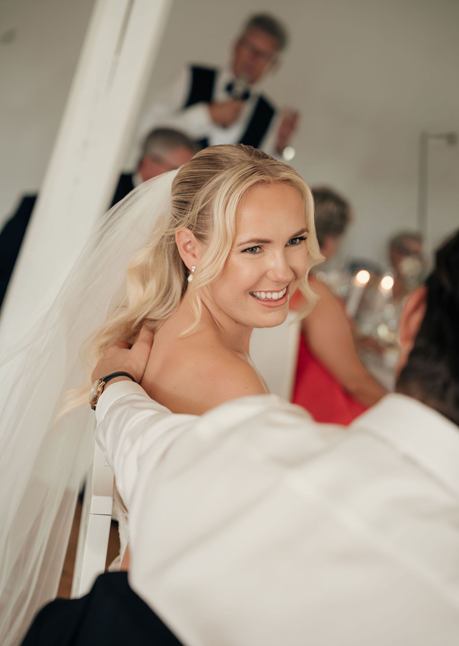 Smiling bride with wavy blonde hair and veil is embraced by a guest during the wedding reception.