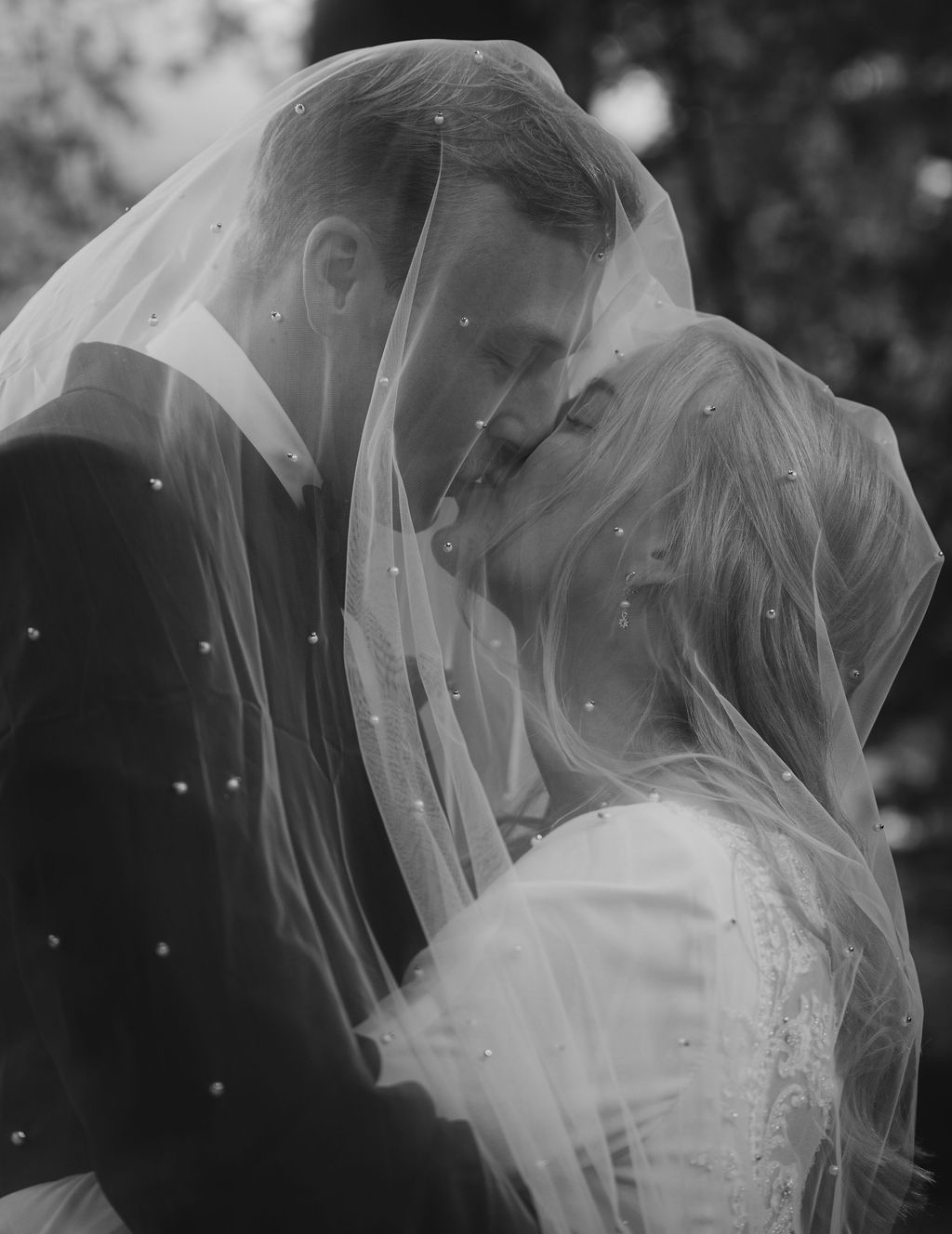 A romantic black and white wedding photograph showing a couple sharing an intimate moment under a delicate veil.