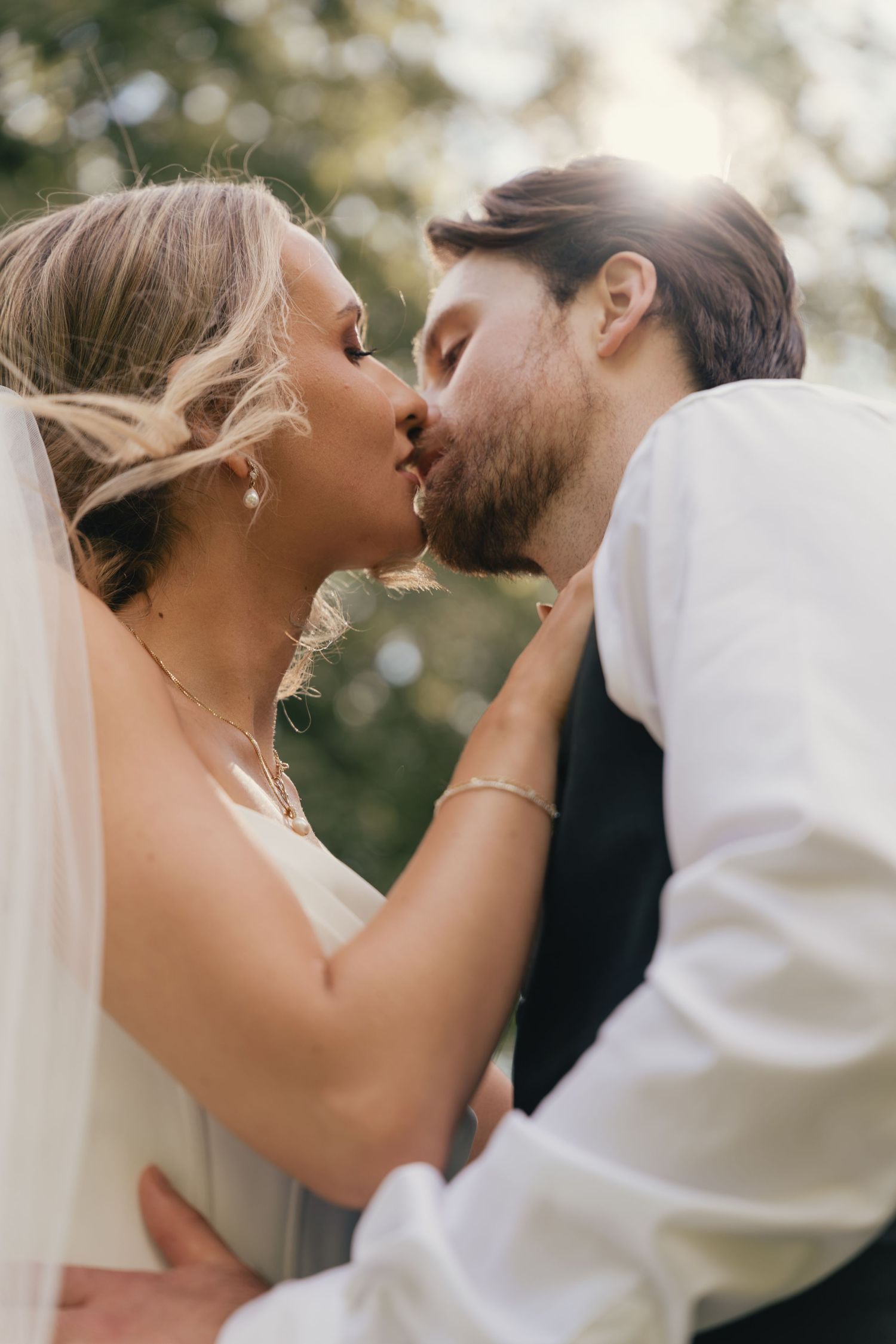 Bride and groom sharing a romantic kiss outdoors with golden sunlight glowing behind them.
