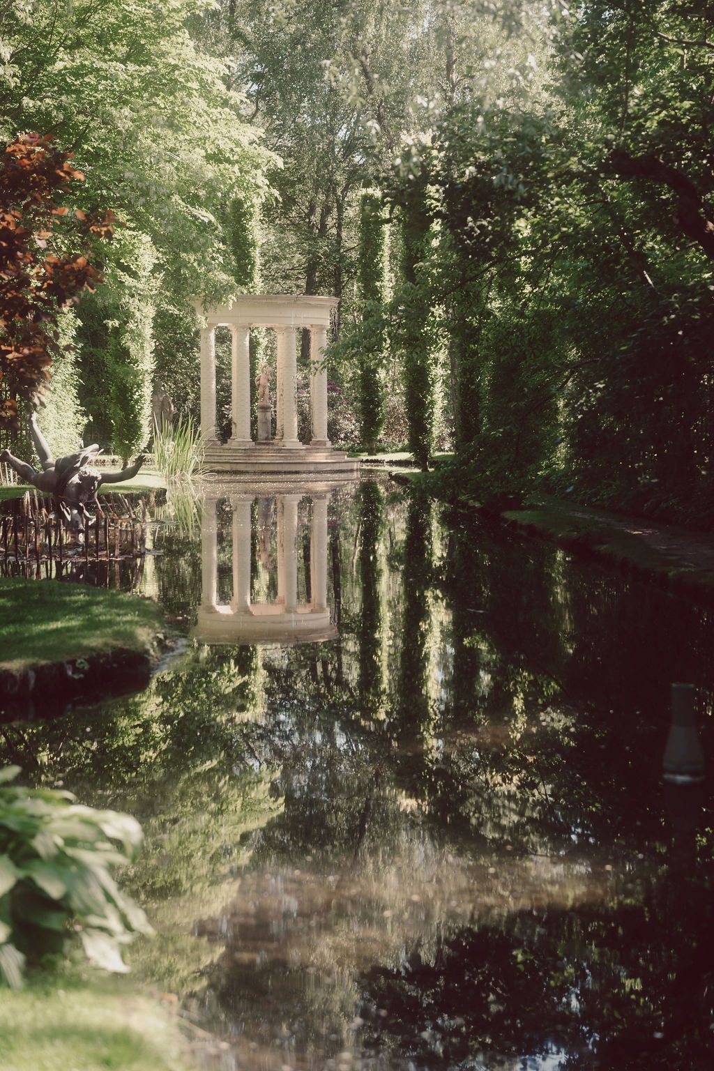 Scenic garden pond reflecting classical architecture and lush greenery in a tranquil setting.