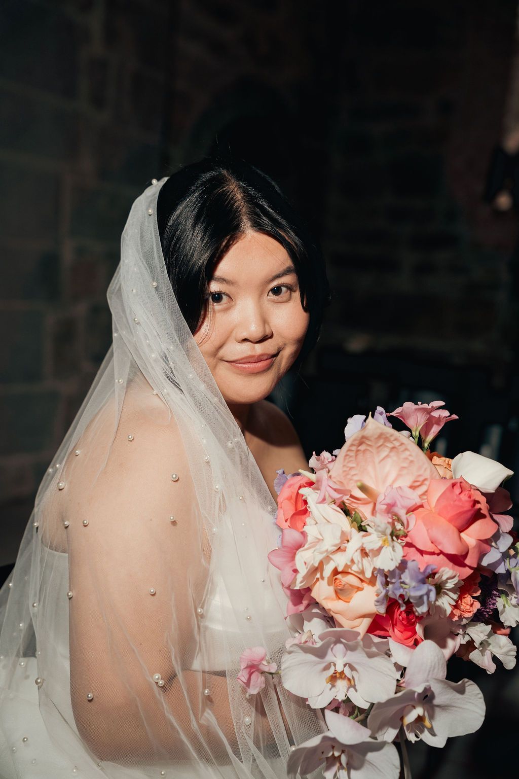 Close-up shots of a bride holding an elegant coral and white bouquet with a delicate veil in a dark setting.