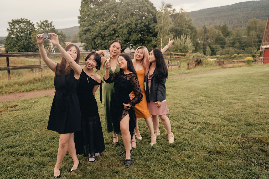 Friends in casual attire enjoying a fun moment together on a grassy hillside with mountains in the background.