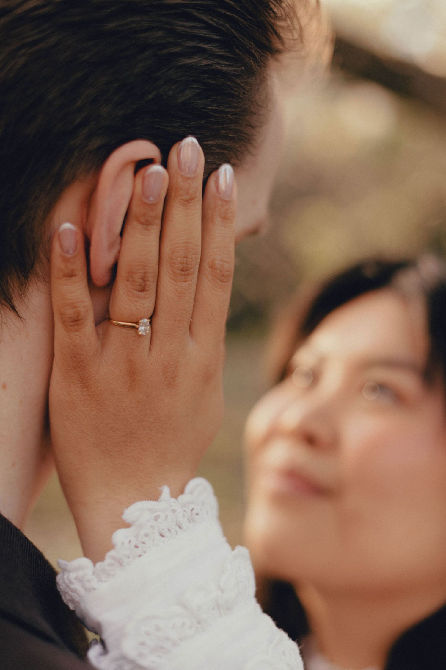 Close-up view of hands with a wedding ring against a soft blurred background with white lace details.