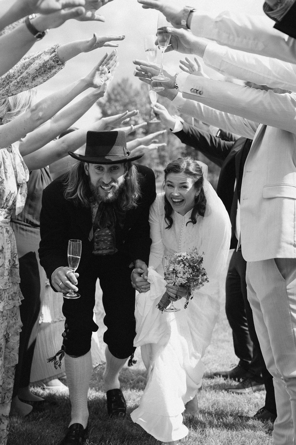 A joyful wedding party performs the limbo dance outdoors with guests holding up their arms to create a tunnel.