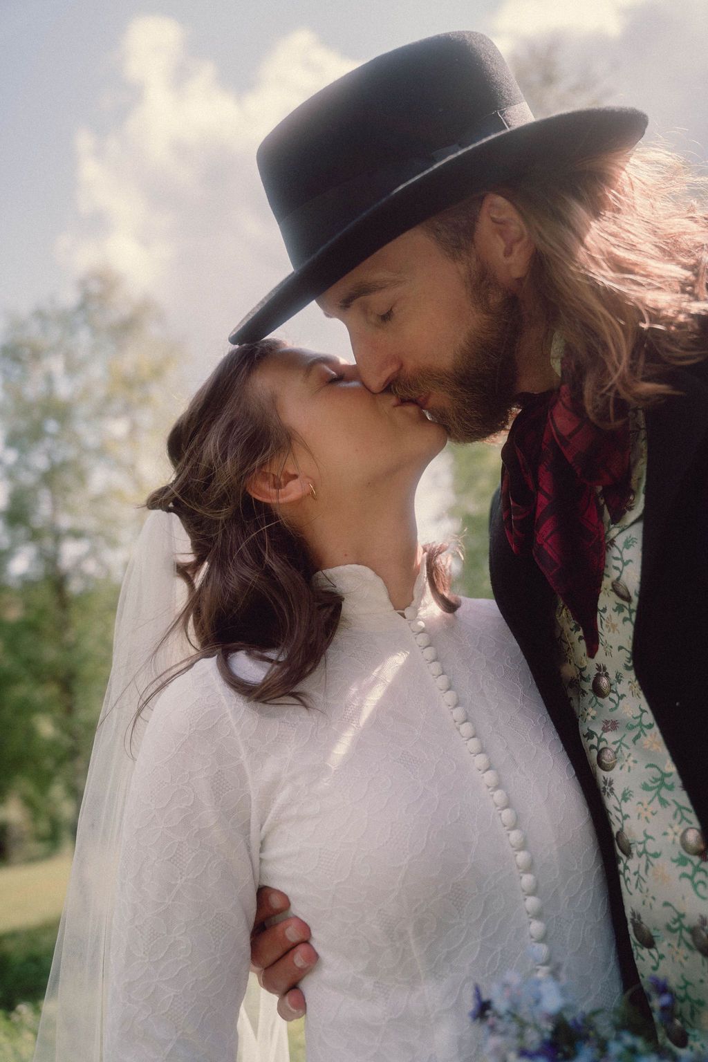 A romantic moment captured between newlyweds in vintage-inspired wedding attire against a natural outdoor setting.