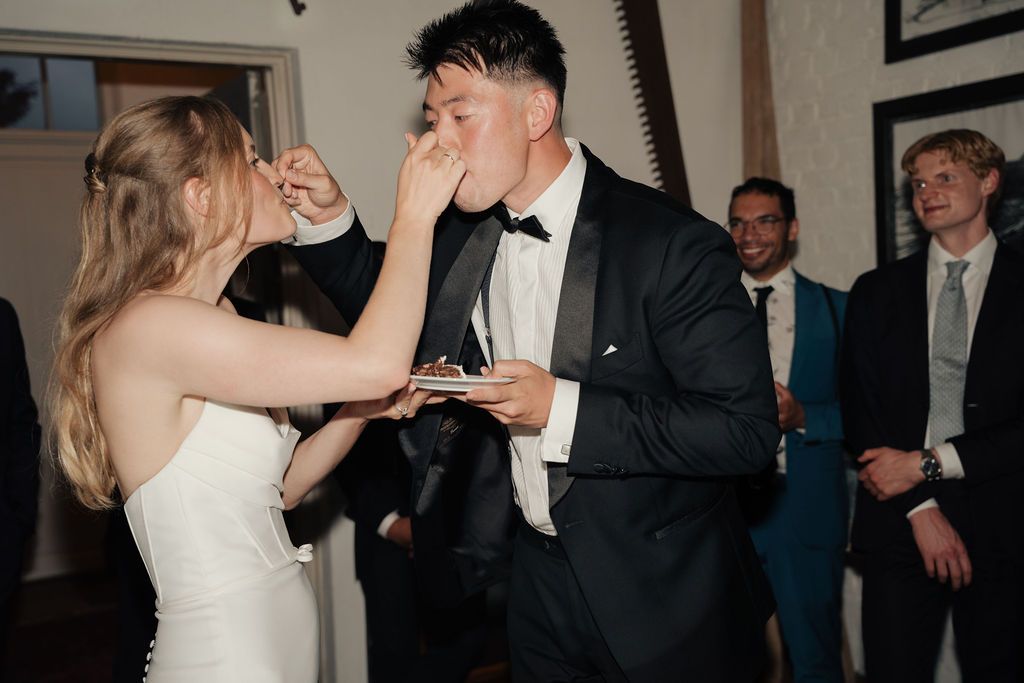 A bride and groom share a celebratory toast at their wedding reception while guests look on in the background.