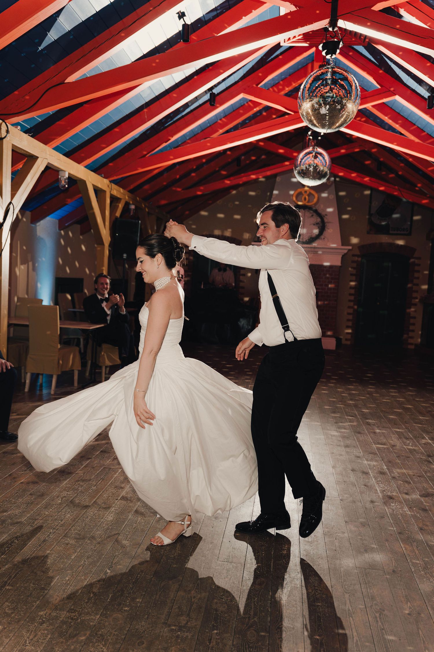 Bride and groom share first dance in decorated barn venue with disco balls and colorful striped ceiling.