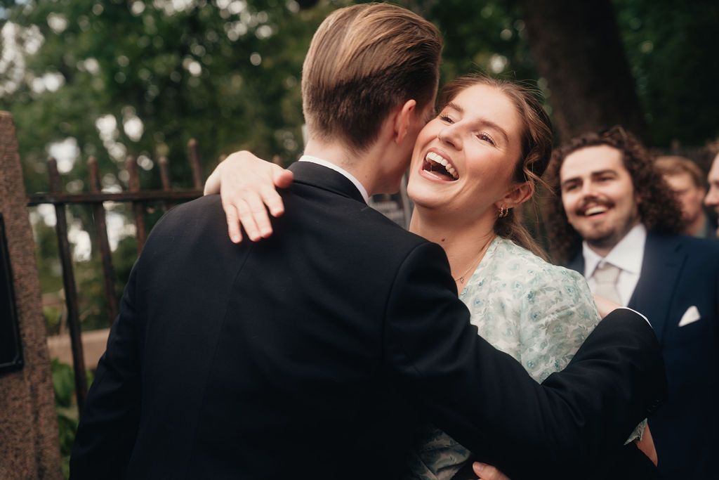 A couple shares a joyful embrace surrounded by wedding guests during an outdoor celebration.