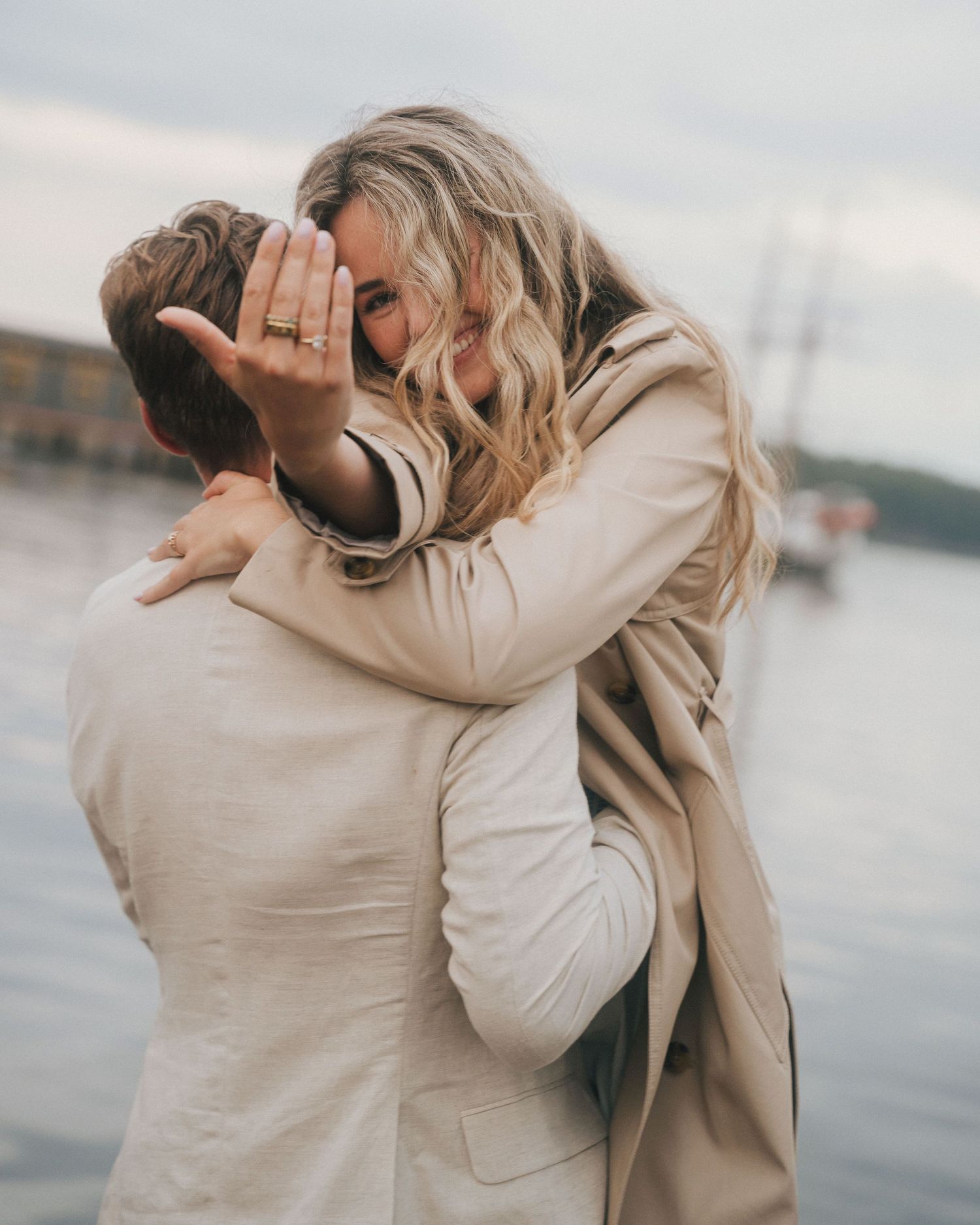 A couple in beige outerwear embraces intimately by the waterfront in a series of candid romantic moments.