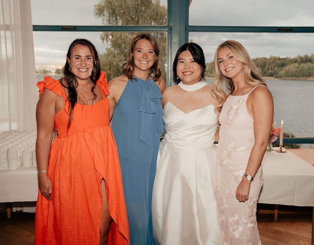 A group in coordinating dresses in coral orange, blue and white poses together at an outdoor event.