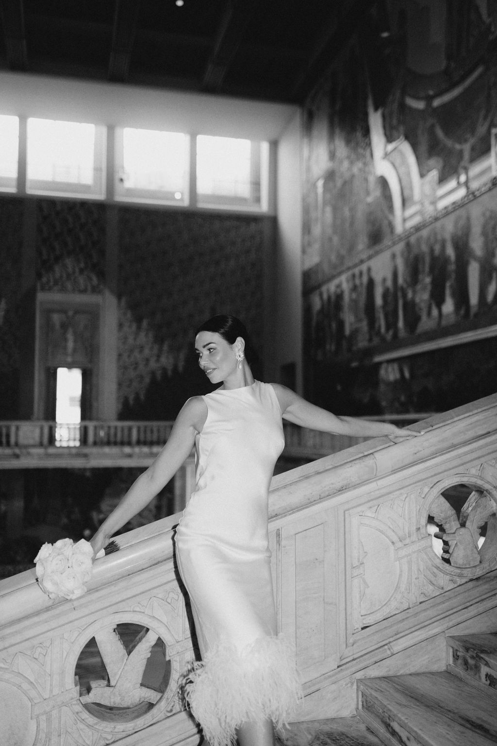 A person in a white dress sits on an ornate staircase in a vintage black and white photograph.
