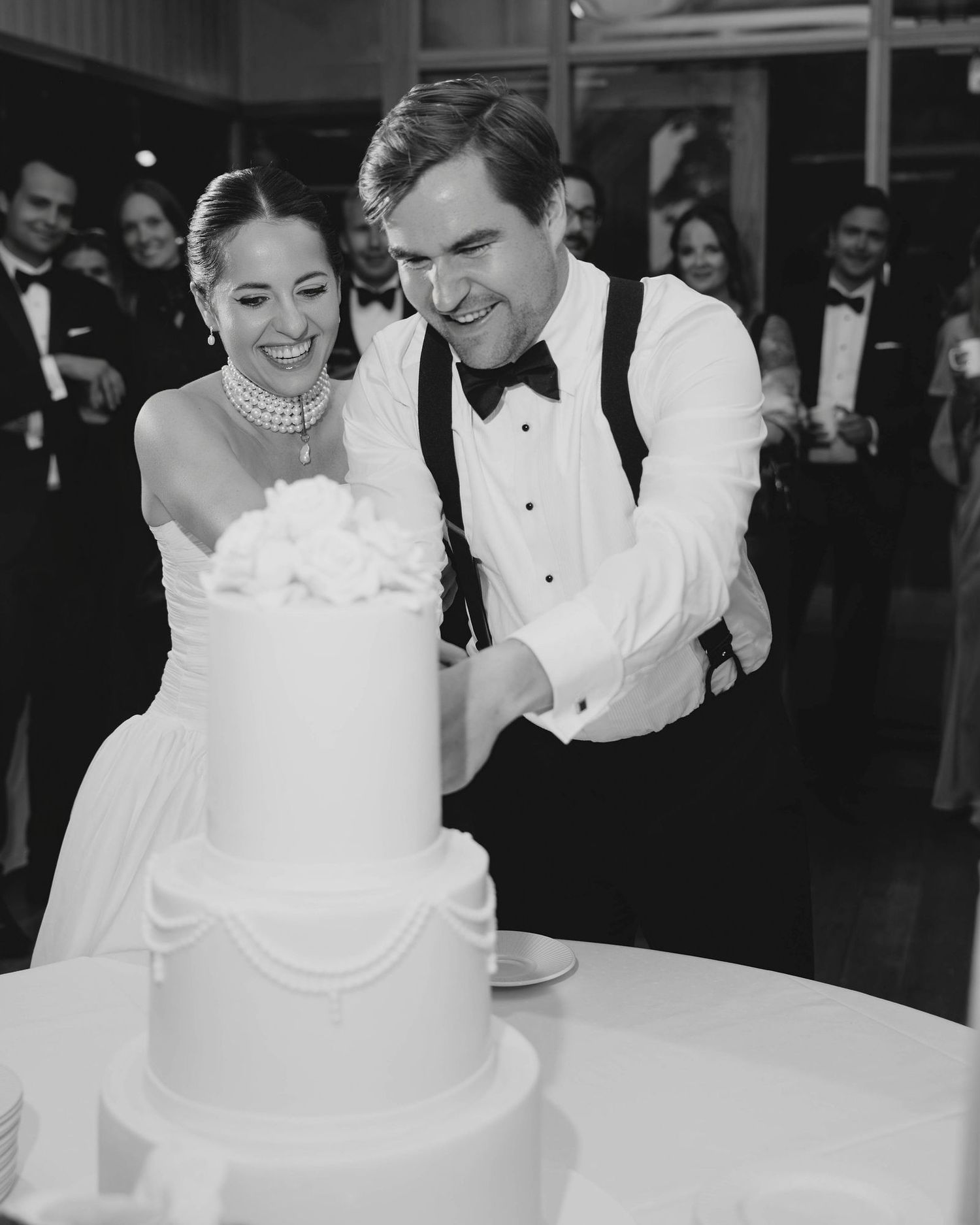 Black and white photo of a bride and groom cutting their elegant tiered wedding cake at their reception.