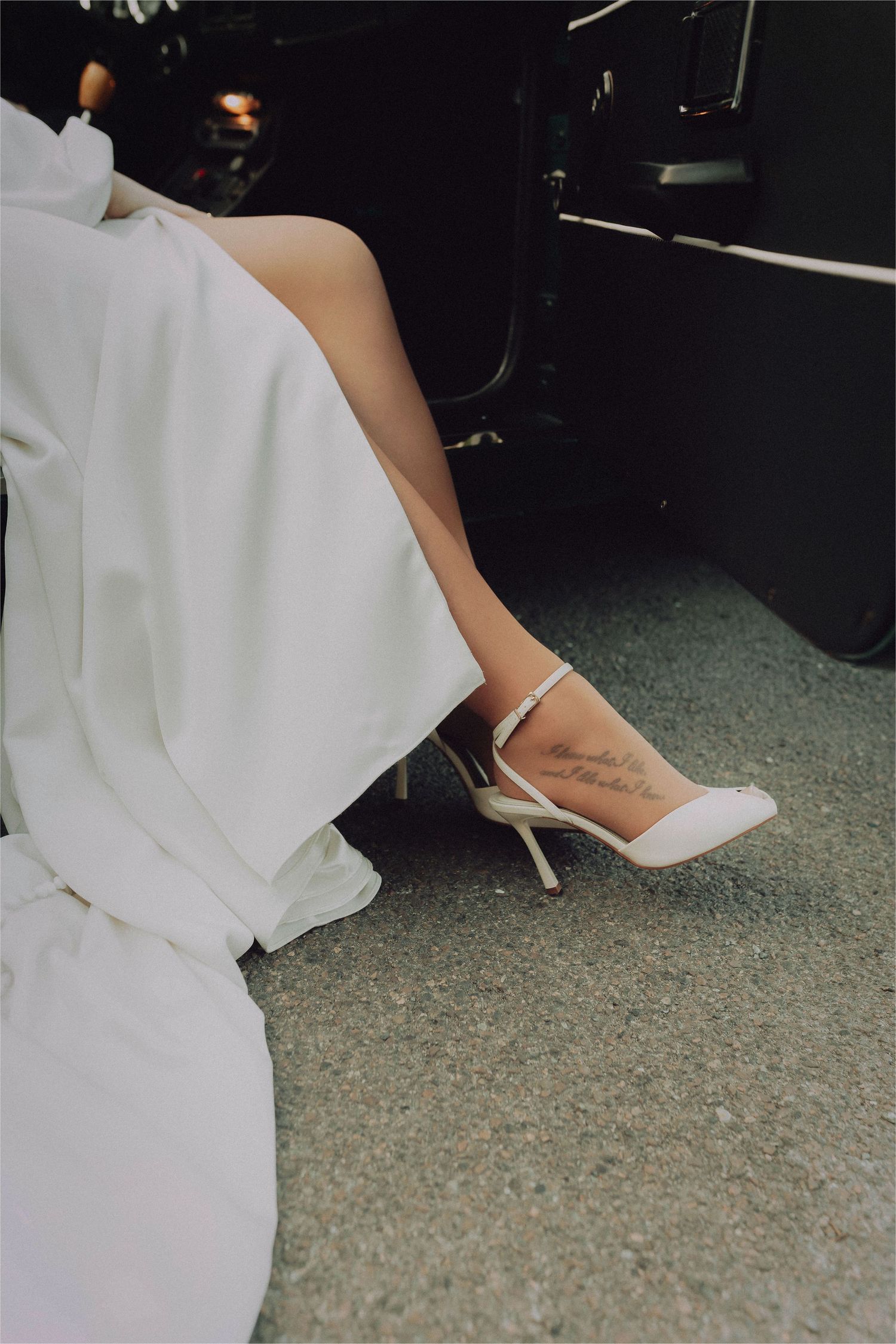 Close-up view of a person's feet wearing elegant white high heel shoes with a flowing white dress.