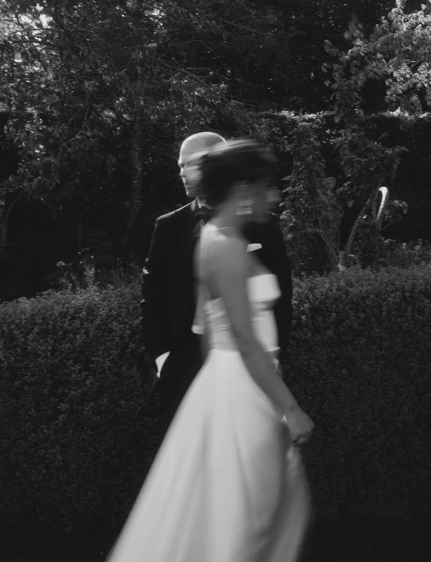 Artistic black and white shot of wedding party members walking through a garden.