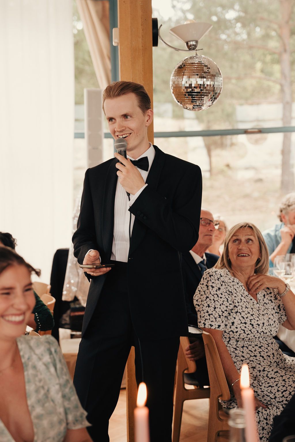 Wedding guests laughing and enjoying themselves at a reception with a disco ball visible in the background.