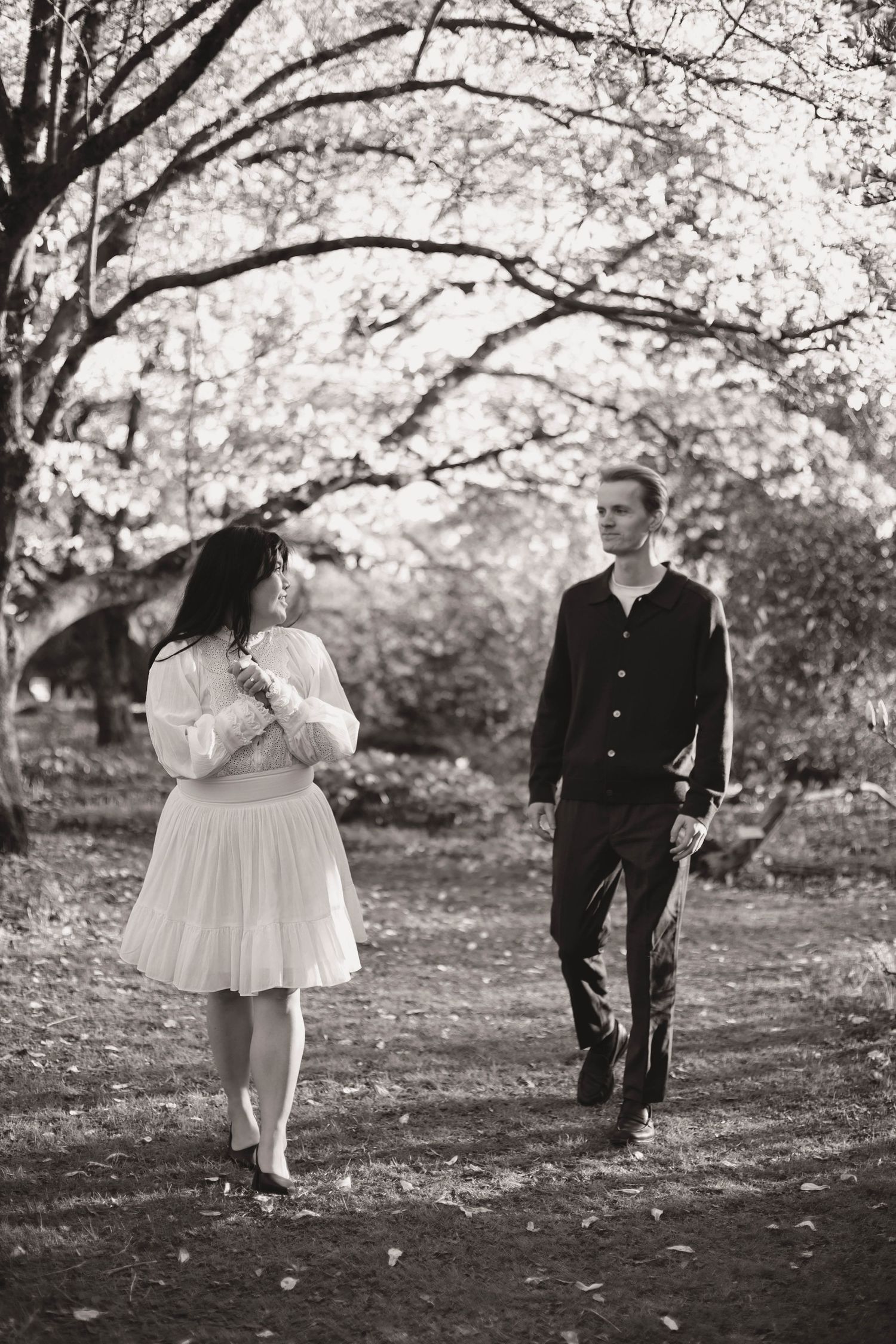 Black and white photo sequence showing a couple walking playfully through fallen autumn leaves under trees.