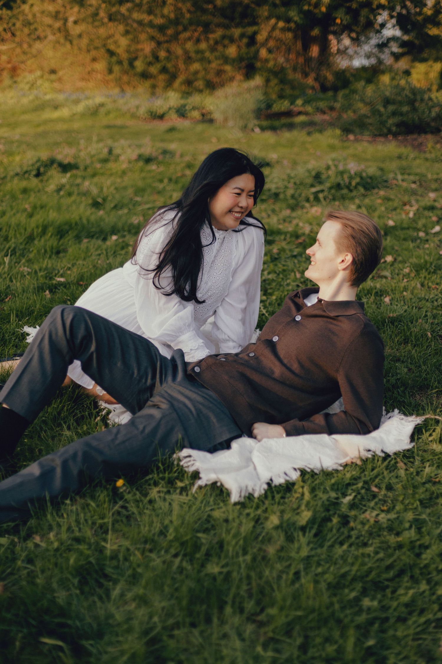 A couple relaxes on a white blanket in a grassy field on a sunny afternoon.
