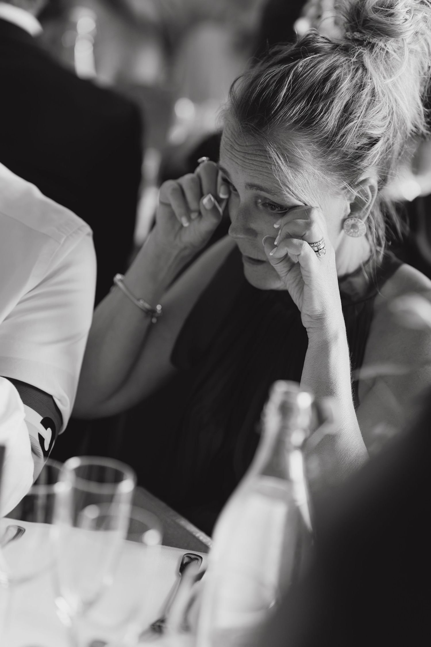 Emotional wedding guest wiping tears at reception table in black and white photo.