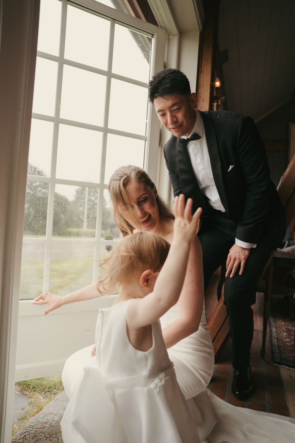 Bride and groom share a playful moment by large windows in a series of candid wedding photos.