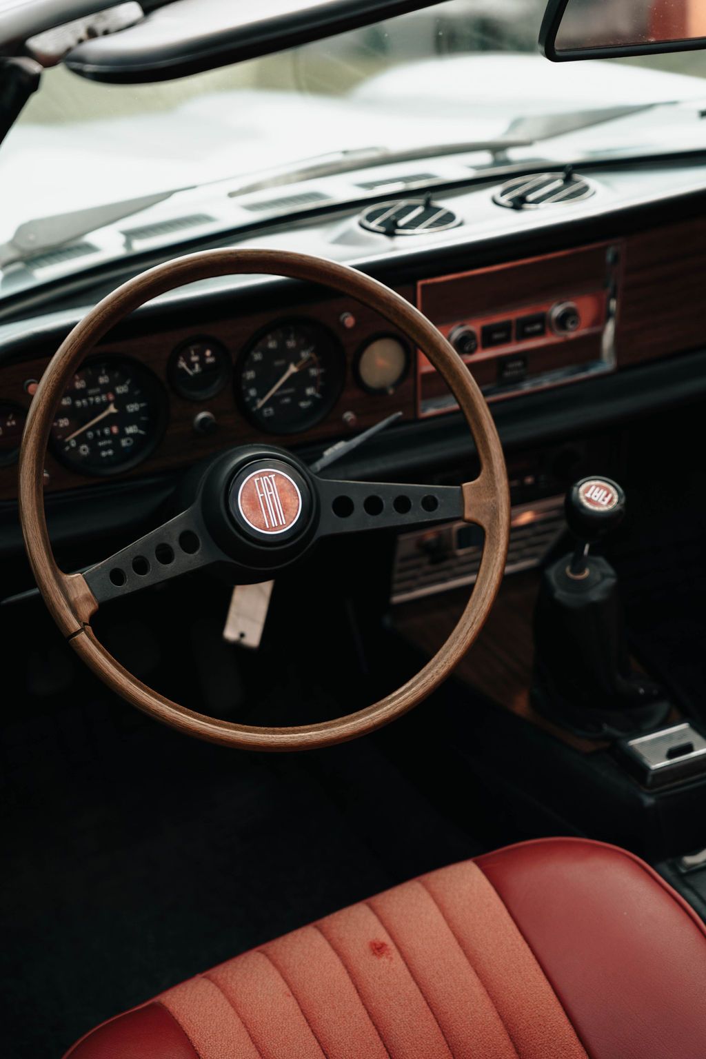 Classic car interior featuring a wooden steering wheel and red leather seats with vintage dashboard instrumentation.
