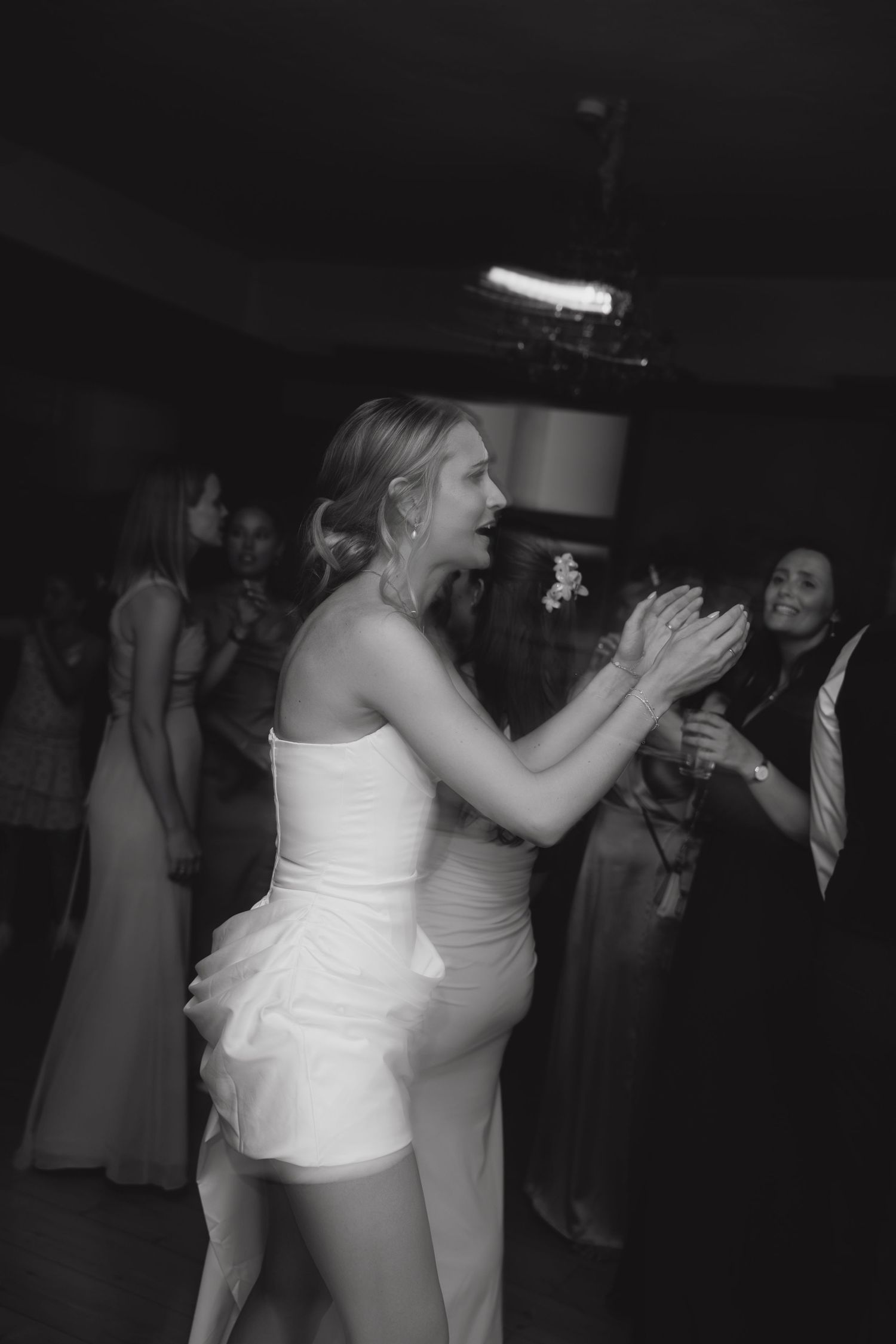 Bride in white mini dress dancing and clapping joyfully at wedding reception.