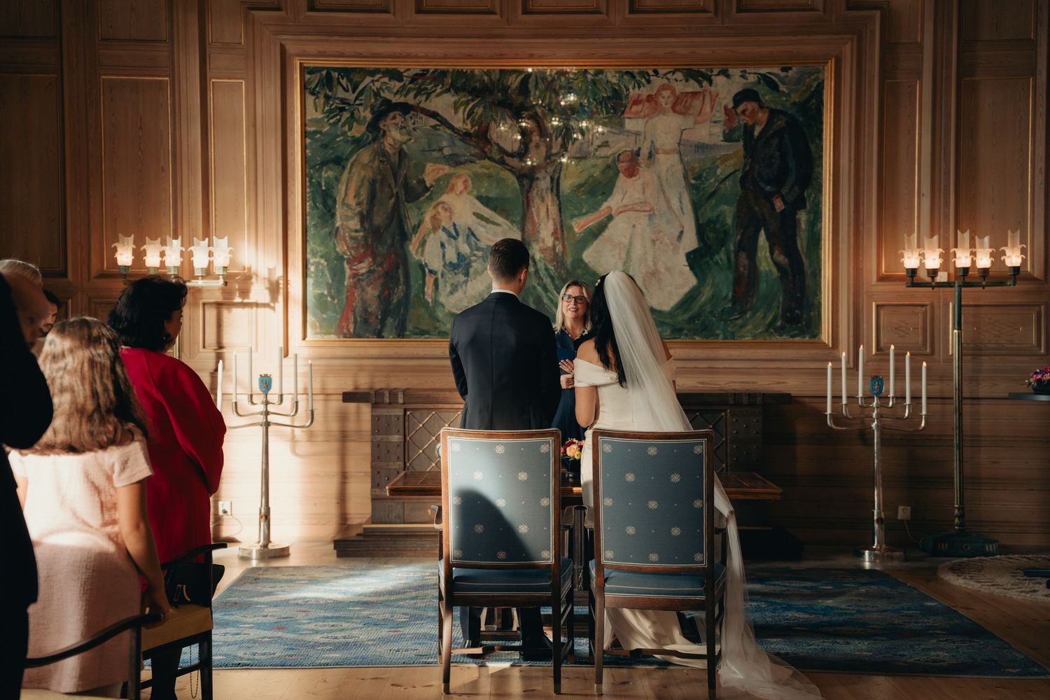 Couple sits in ornate room with candlelight and large decorative wall mural during intimate ceremony.