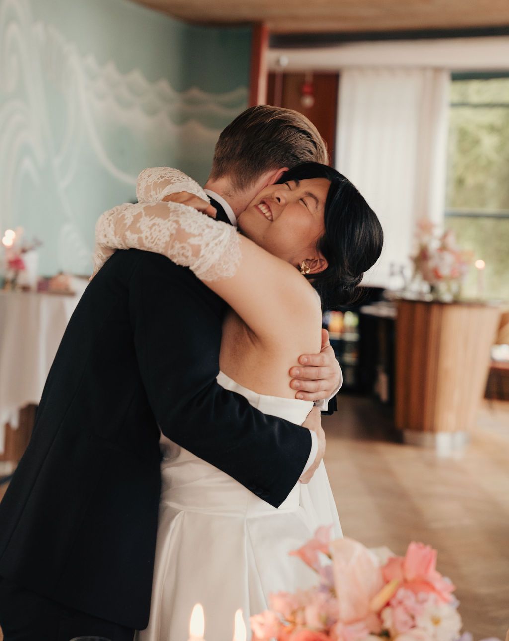 A romantic couple in wedding attire share an intimate dance moment in a sunlit indoor venue.