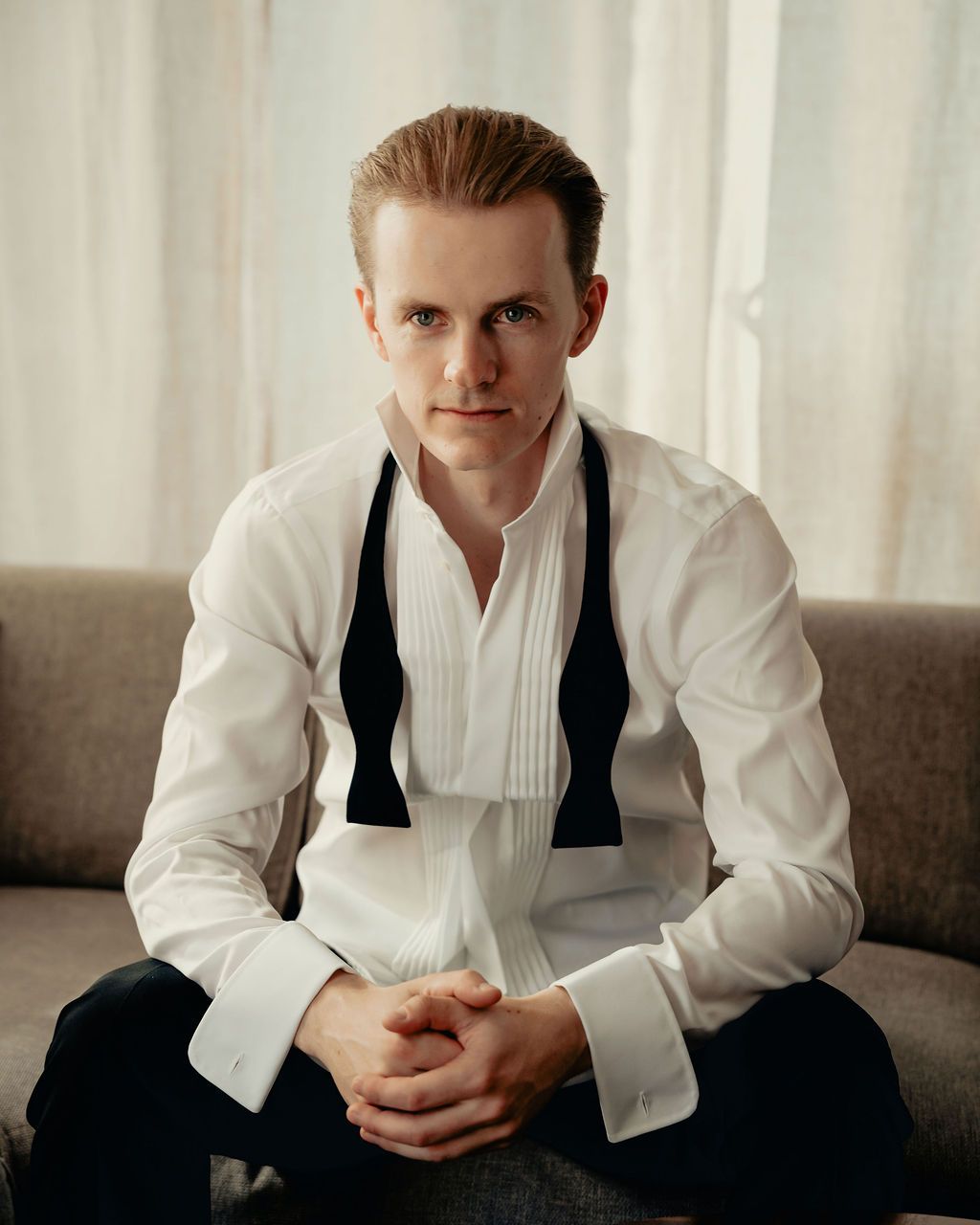 A person in a white dress shirt and dark vest sits in contemplative poses against a light background.