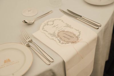 Elegant wedding place setting with silverware, white plate, and decorative menu card on white tablecloth.