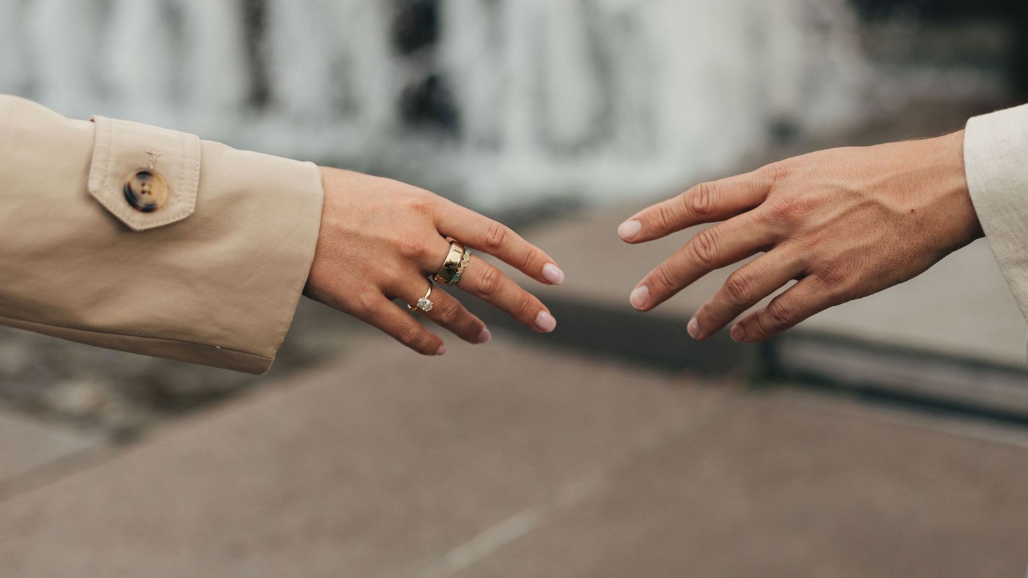 Two hands reaching towards each other against a blurred background, with one hand wearing a beige sleeve.