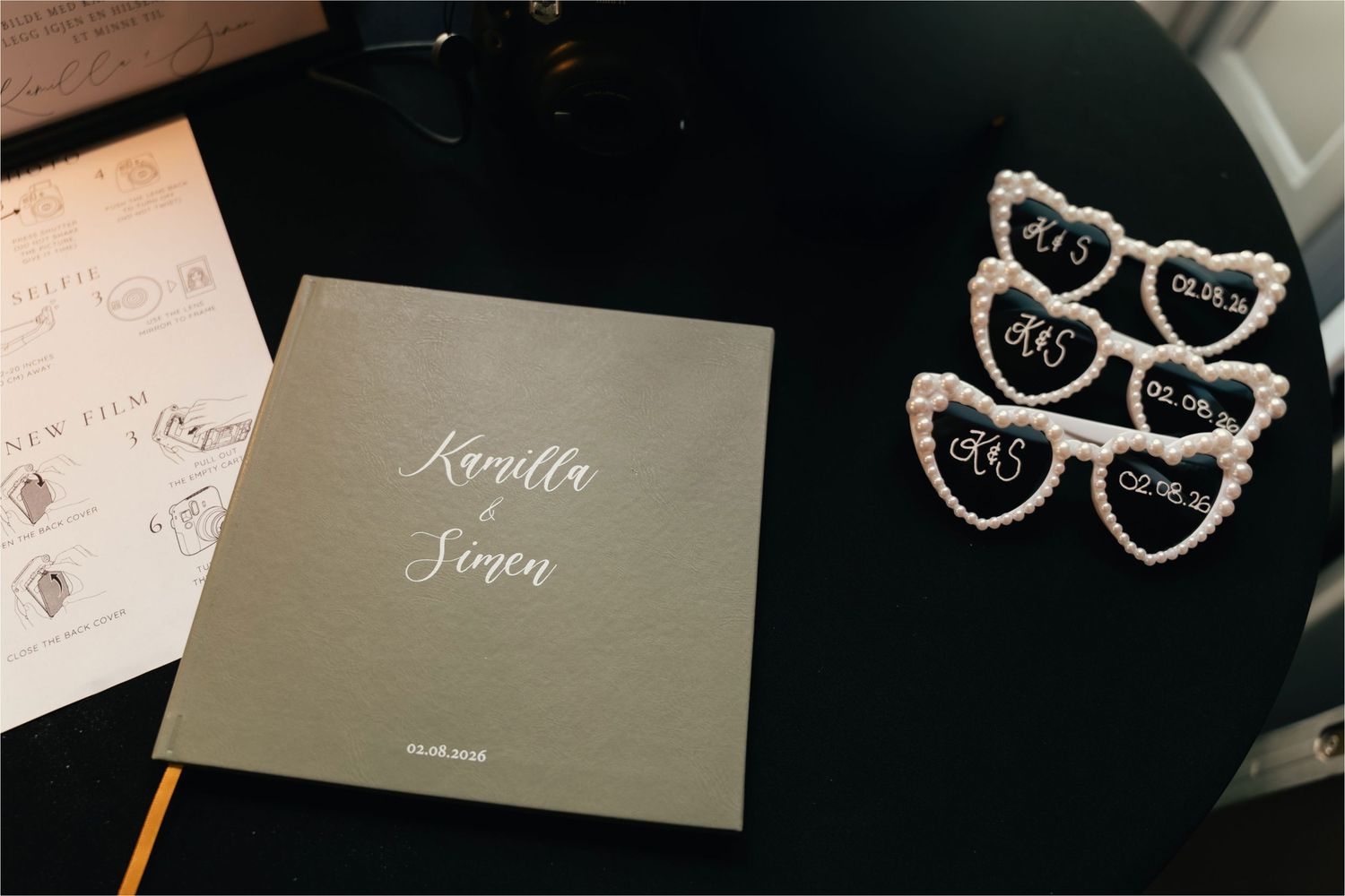 A gray wedding guest book beside pearl heart-shaped table number holders on a dark surface.