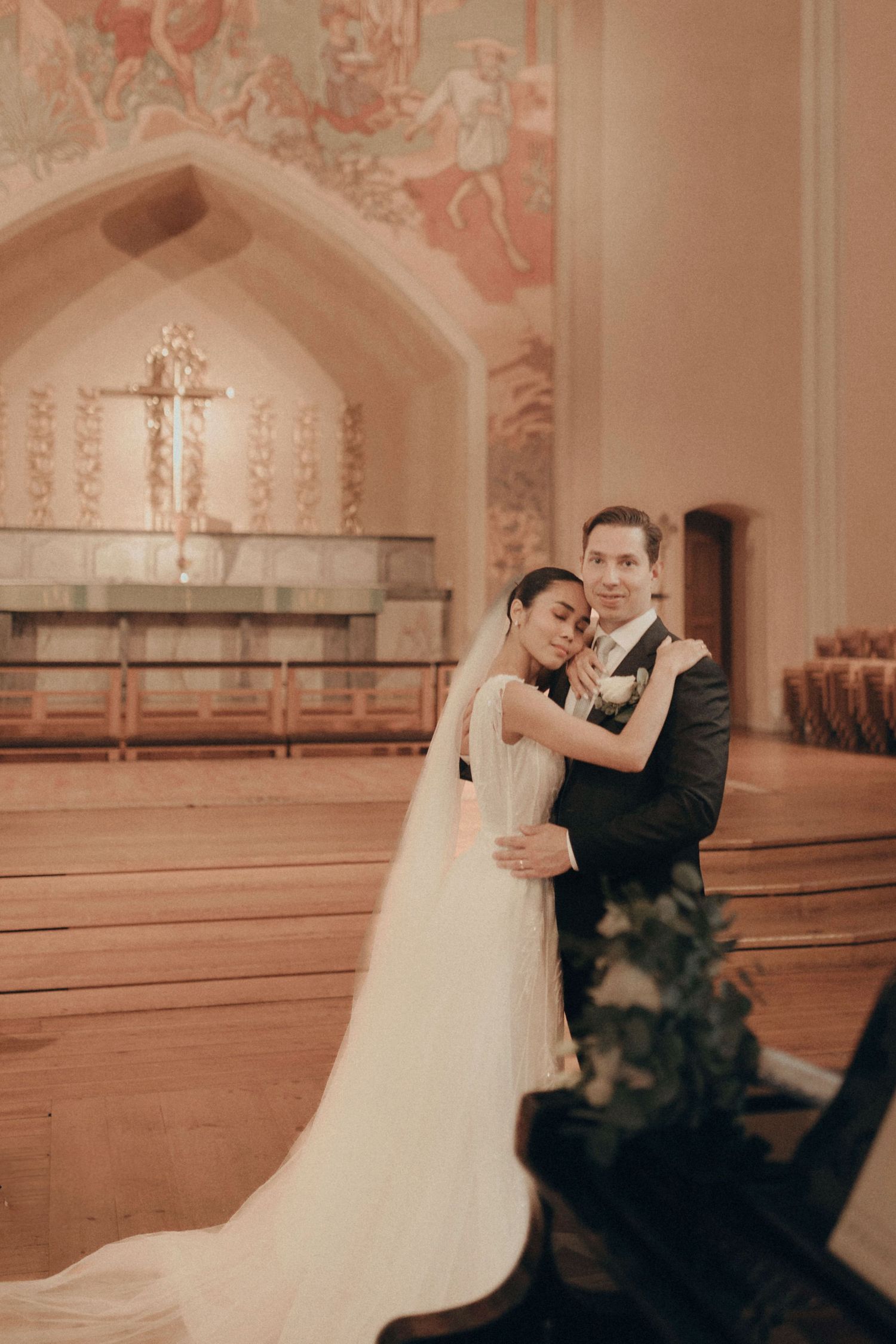 A couple shares an intimate dance moment in an elegant church setting with peach-colored walls and ornate decor.
